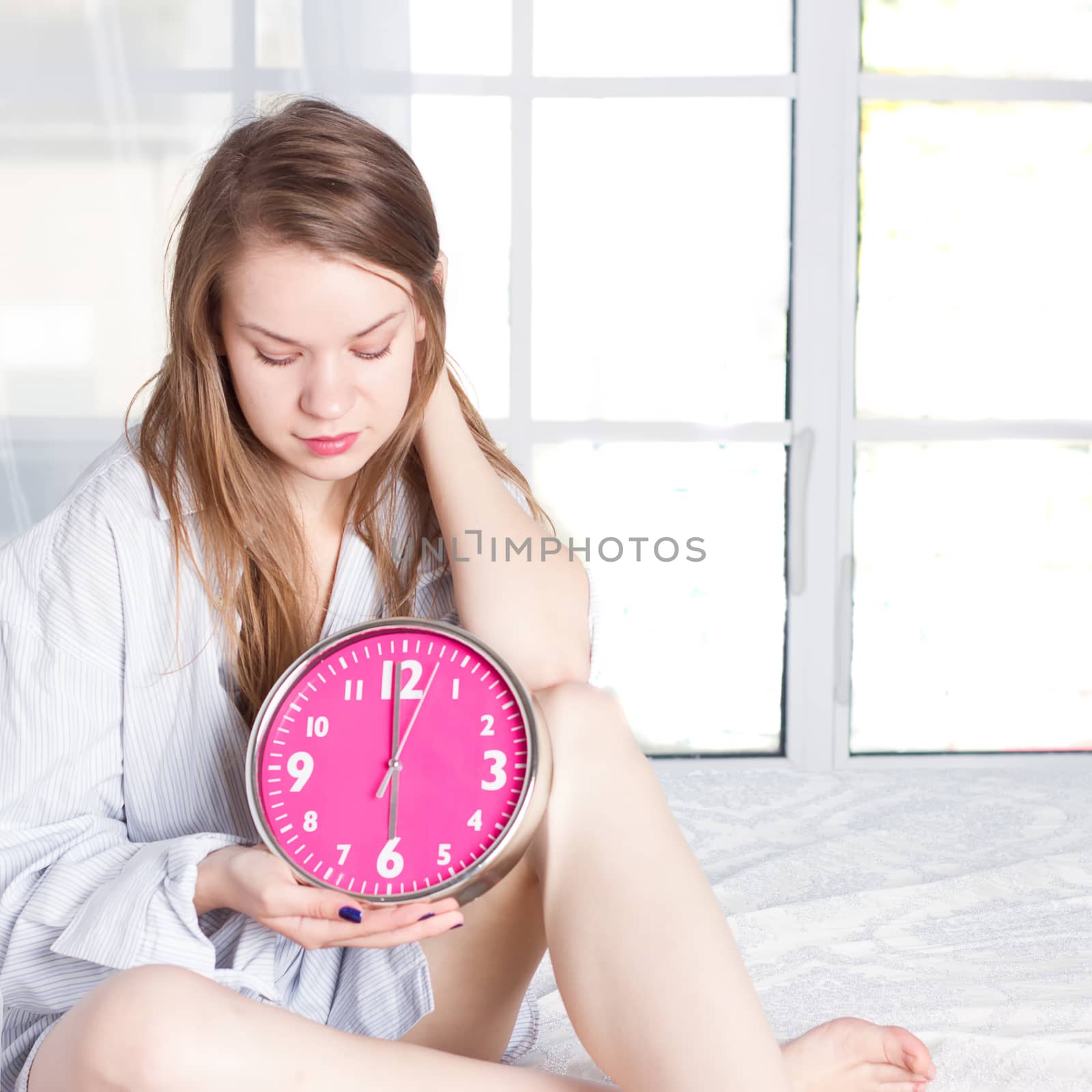 Young woman with alarmclock on the bed at the morning
