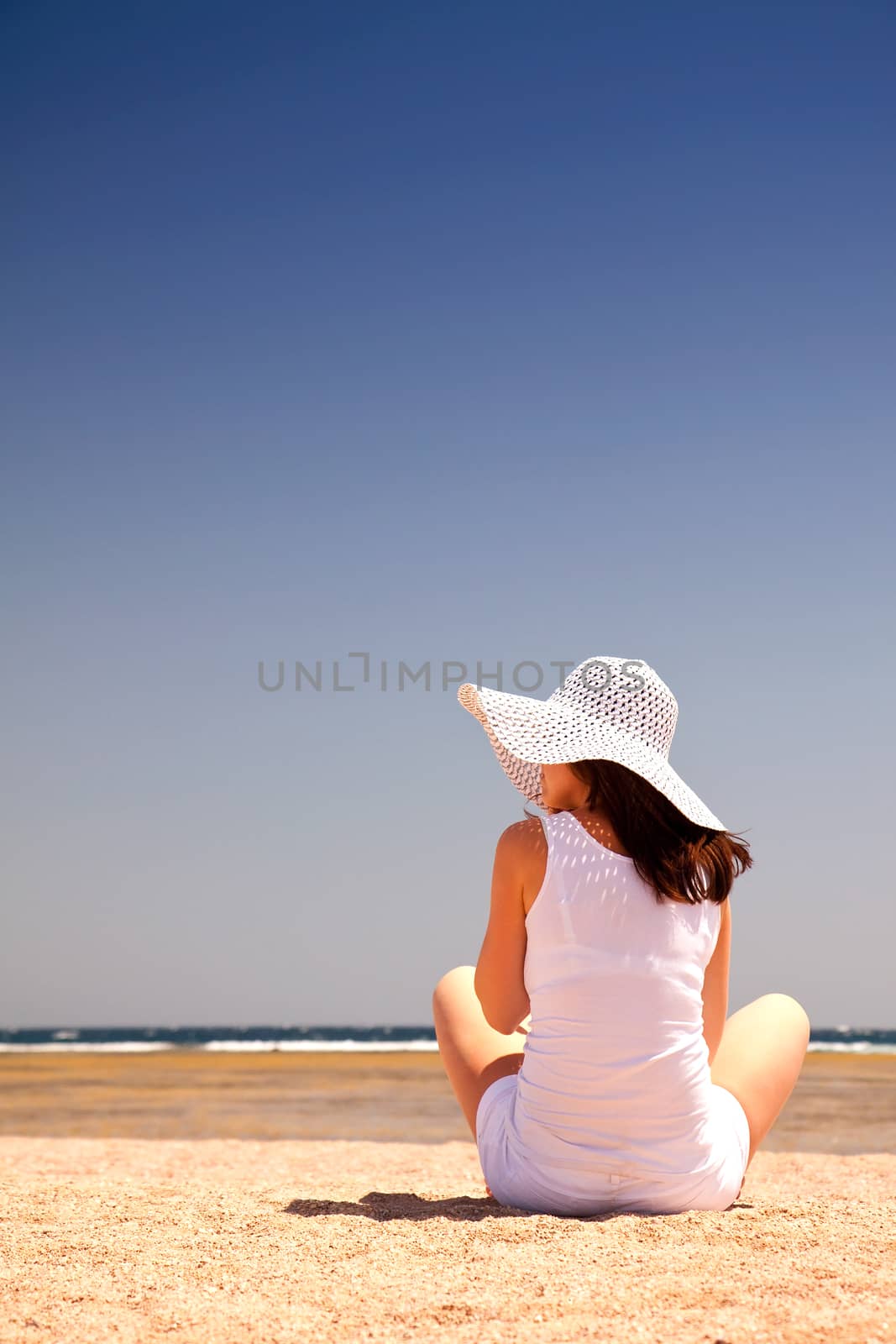 Young woman sitting back on the sand at the beach
