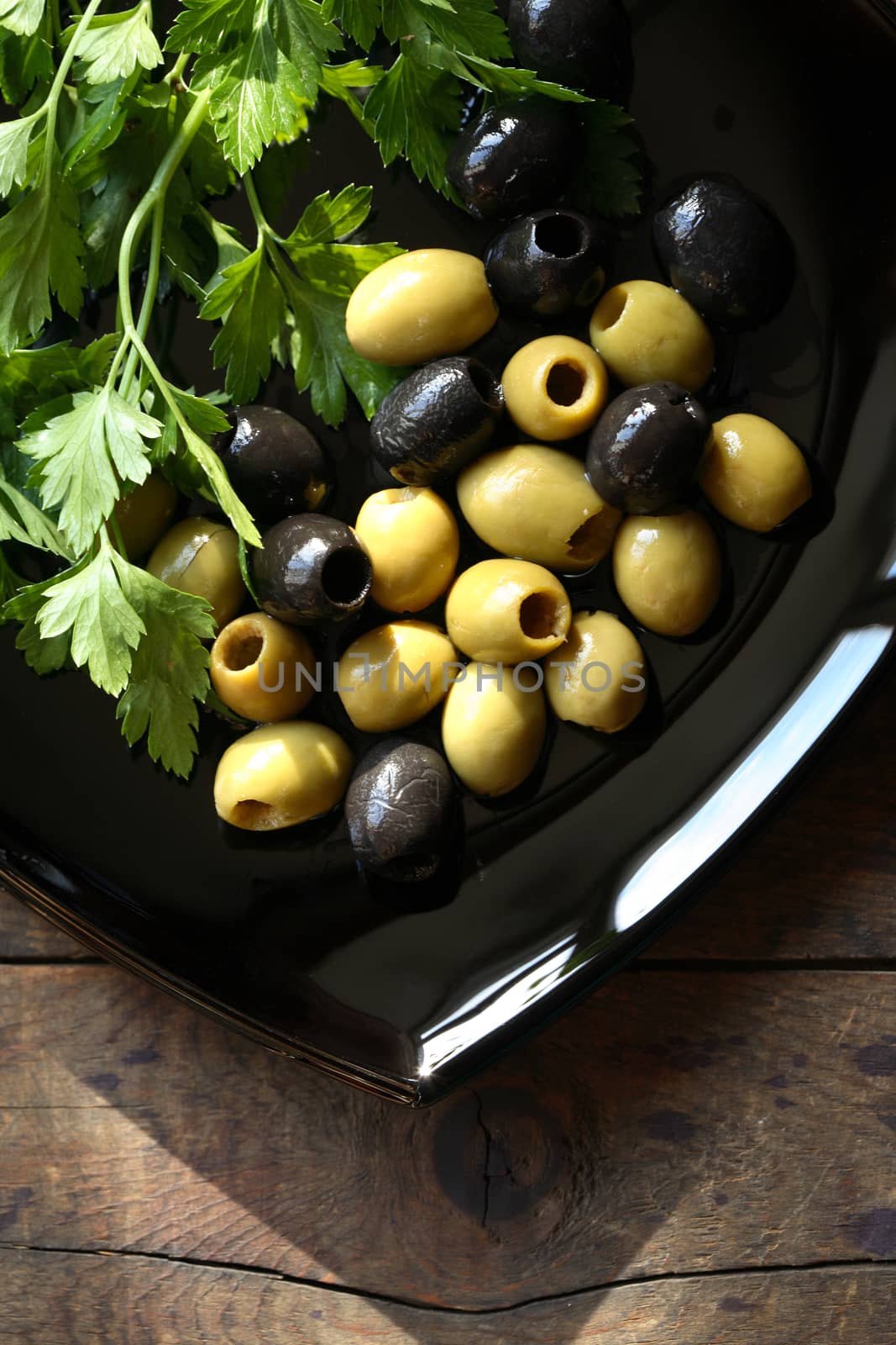 Green and black olives on black plate on nice old wooden table