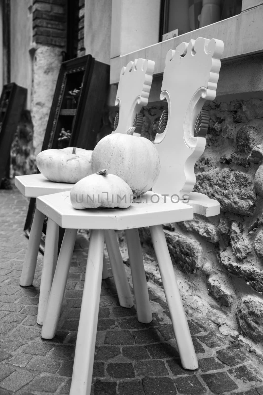two wooden chairs painted white and two white pumpkins against the wall along a street