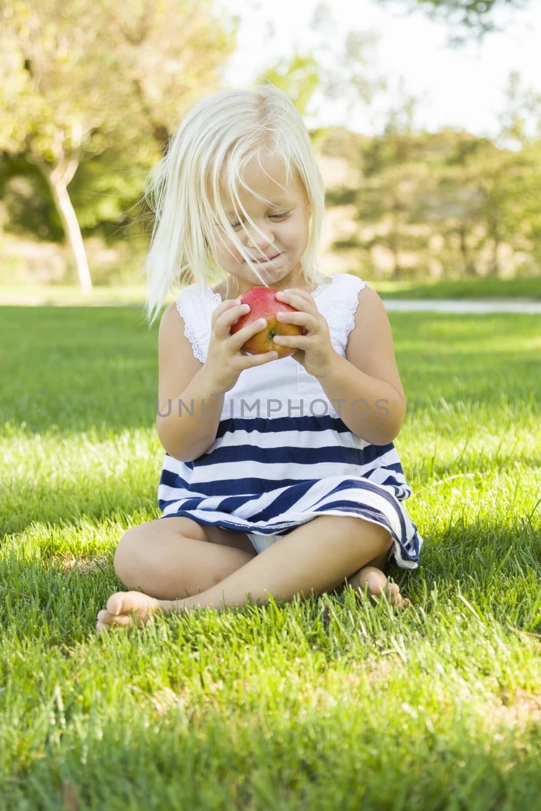 Cute Little Girl Sitting and Eating Apple Outside onThe Grass.