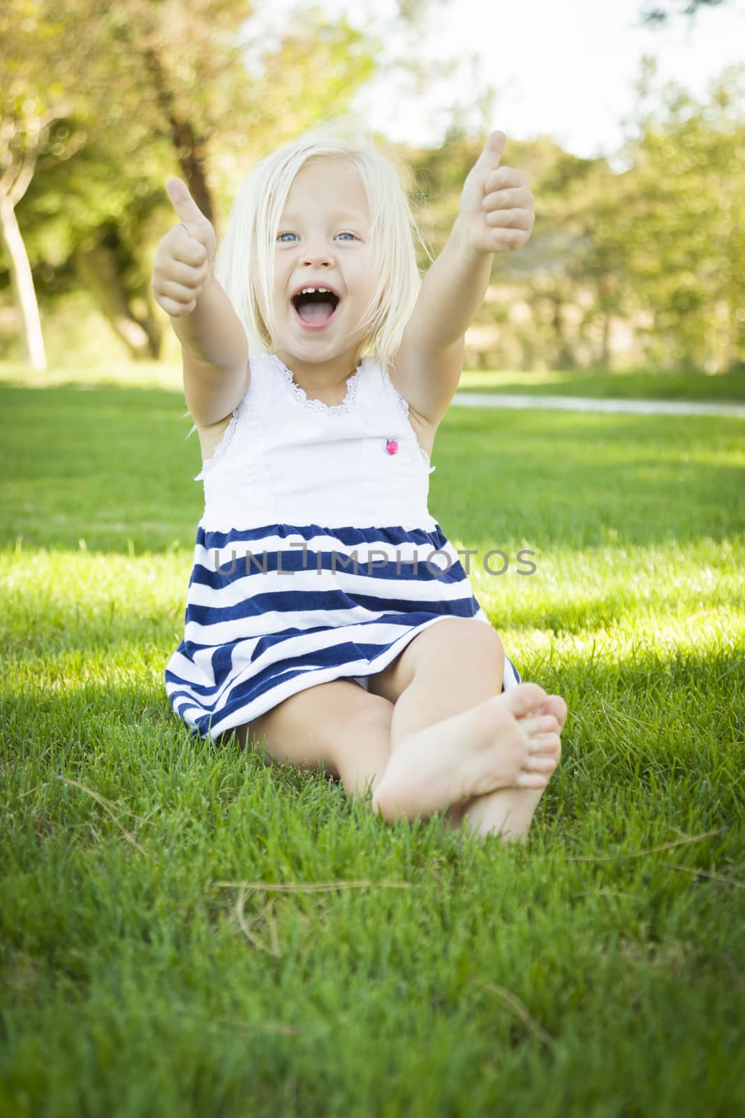 Cute Little Girl with Thumbs Up in the Grass Outside.