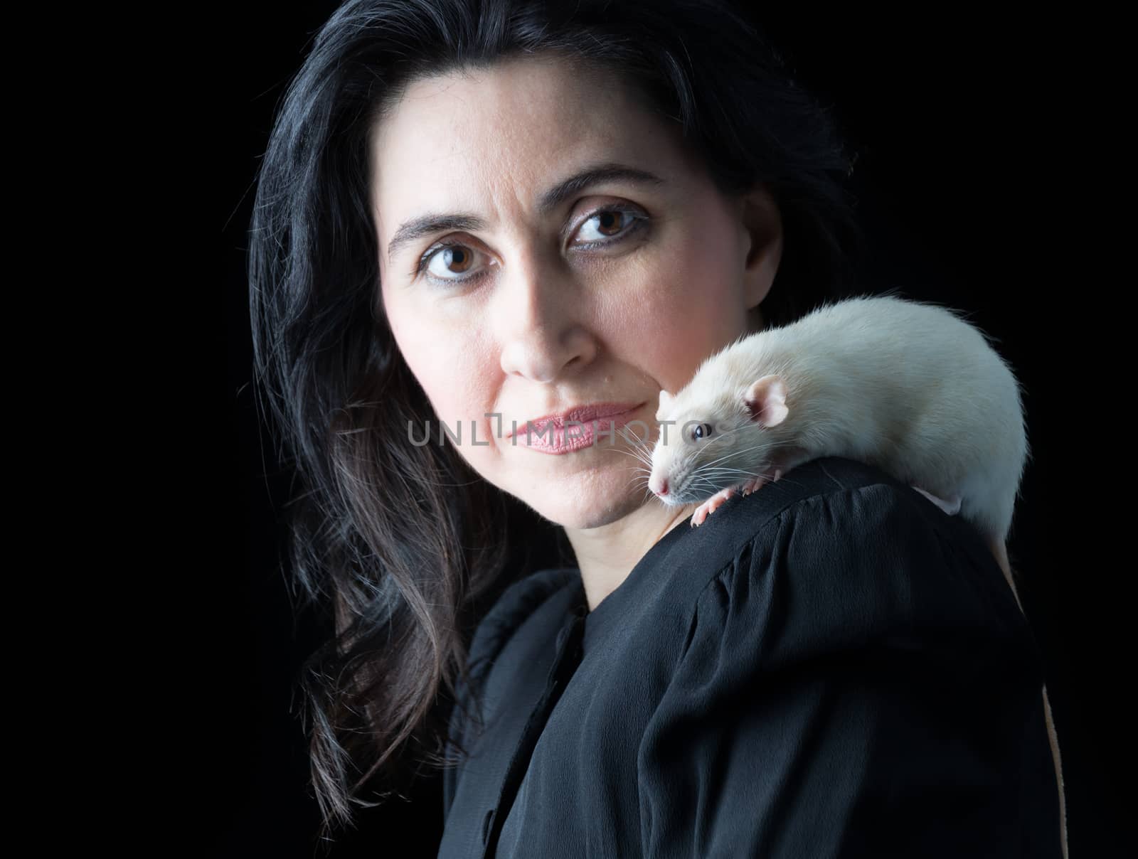 Woman in black standing in front of a black backdrop with a white dumbo rat perched on her shoulder.
