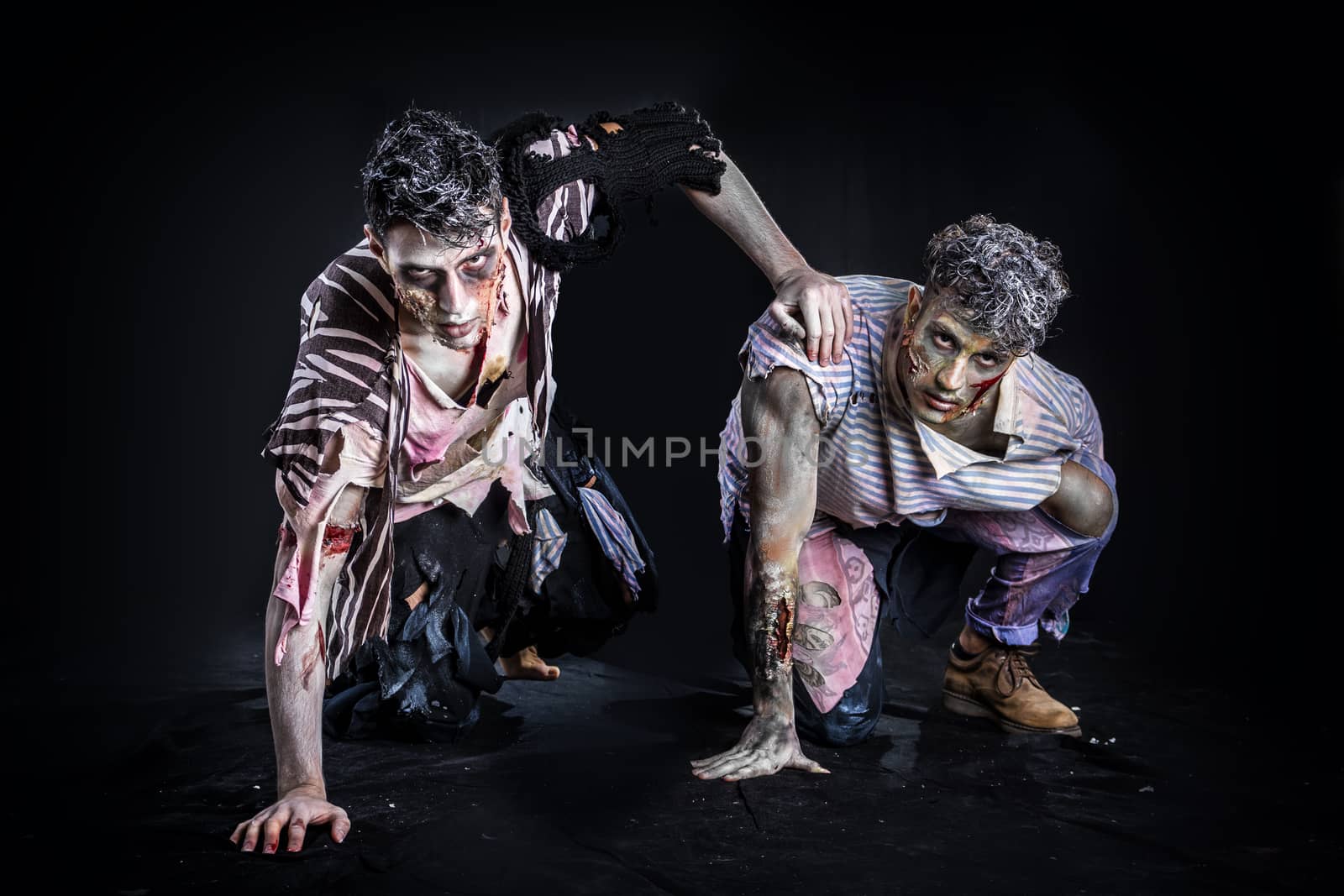 Two male zombies crawling on their knees, on black smoky background, looking at camera. Halloween theme