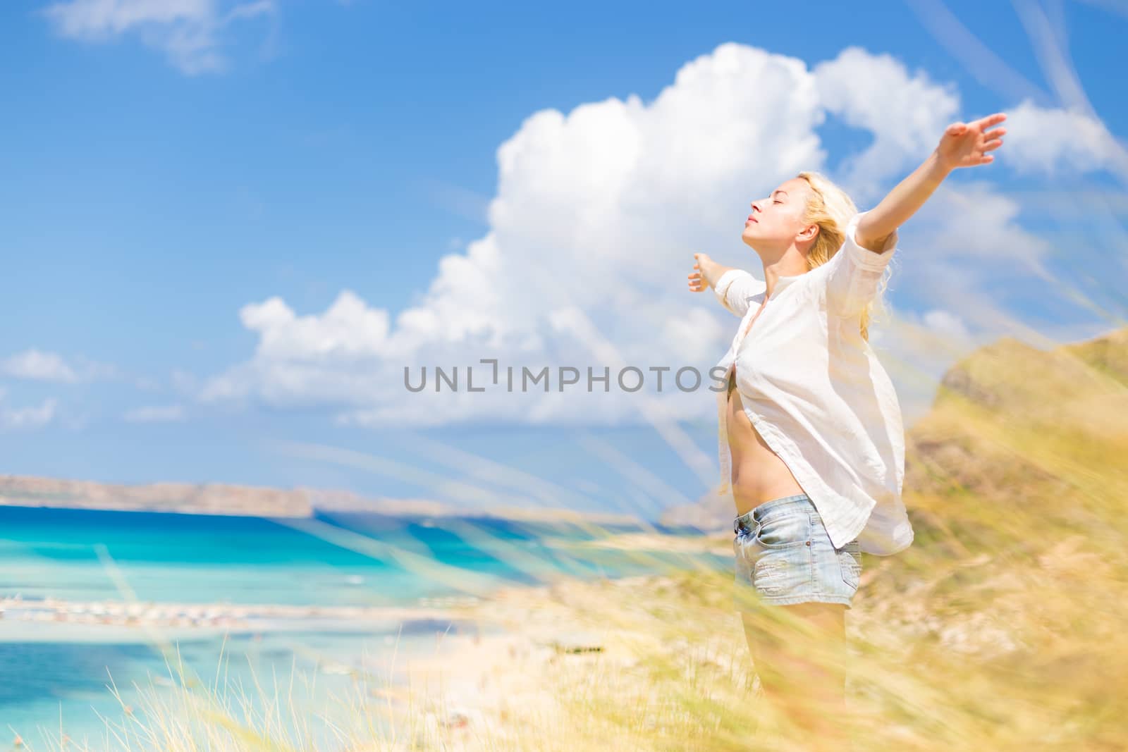 Relaxed woman enjoying freedom and life an a beautiful sandy beach.  Young lady raising arms, feeling free, relaxed and happy. Concept of freedom, happiness, enjoyment and well being.