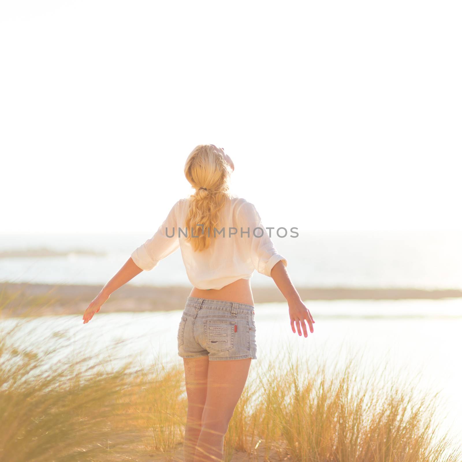Relaxed woman enjoying freedom and life an a beautiful sandy beach.  Young lady feeling free, relaxed and happy. Concept of happiness, enjoyment and well being.  Enjoying Sun on Vacations. Copyspace.