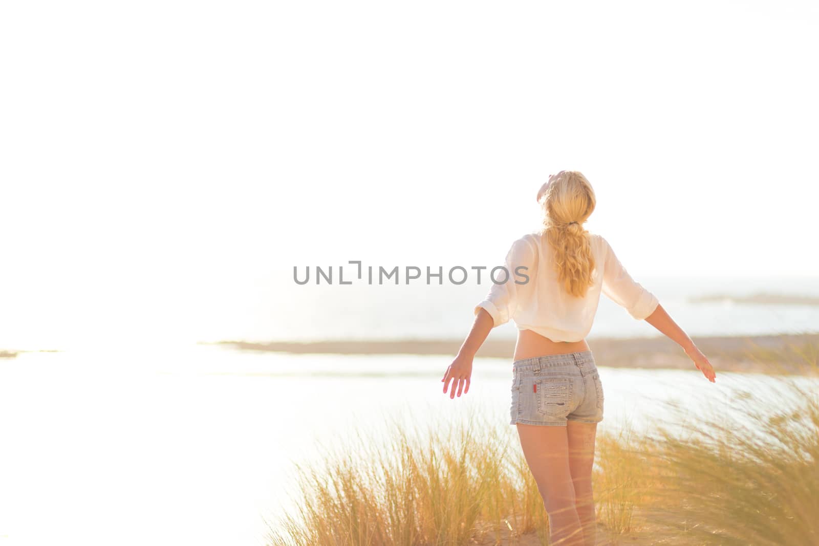 Relaxed woman enjoying freedom and life an a beautiful sandy beach.  Young lady feeling free, relaxed and happy. Concept of happiness, enjoyment and well being.  Enjoying Sun on Vacations. Copyspace.