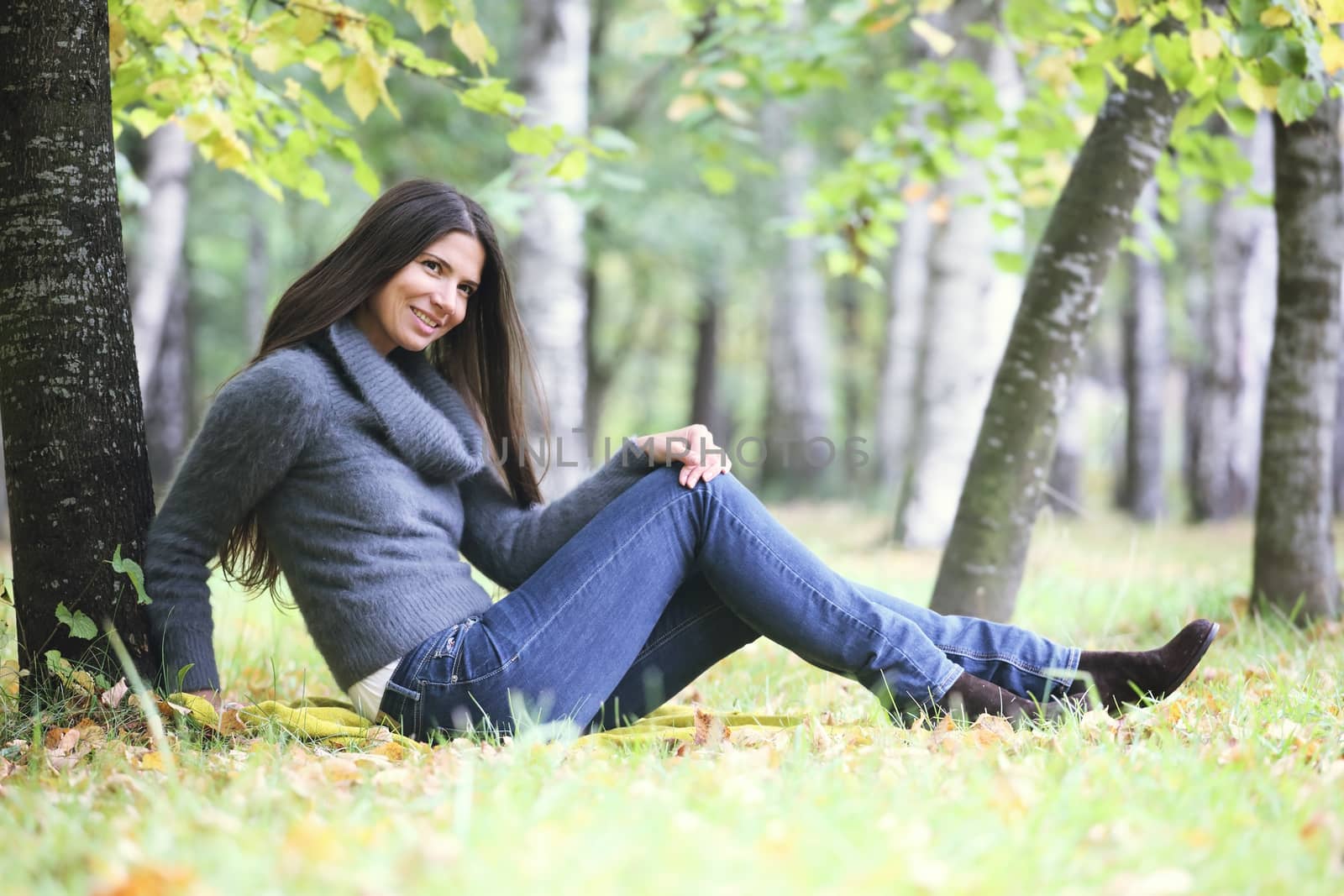 Beautiful brunette woman sitting under the tree in autumn park