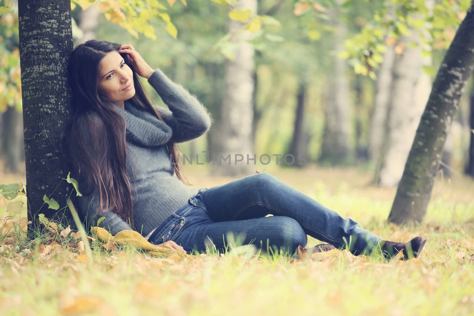 Beautiful brunette woman sitting under the tree in autumn park