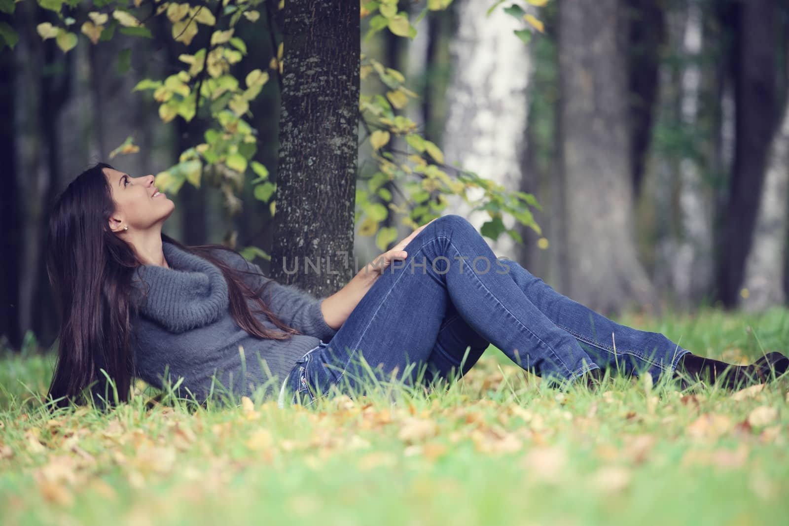 Beautiful brunette woman laying under the tree in autumn park