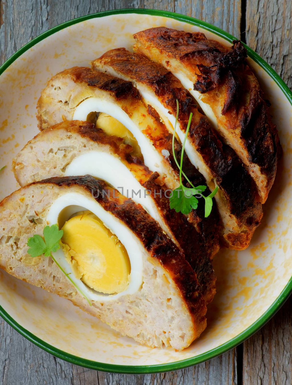 Delicious Slised Meatloaf Stuffed with Boiled Eggs in Bowl closeup on Rustic Wooden background