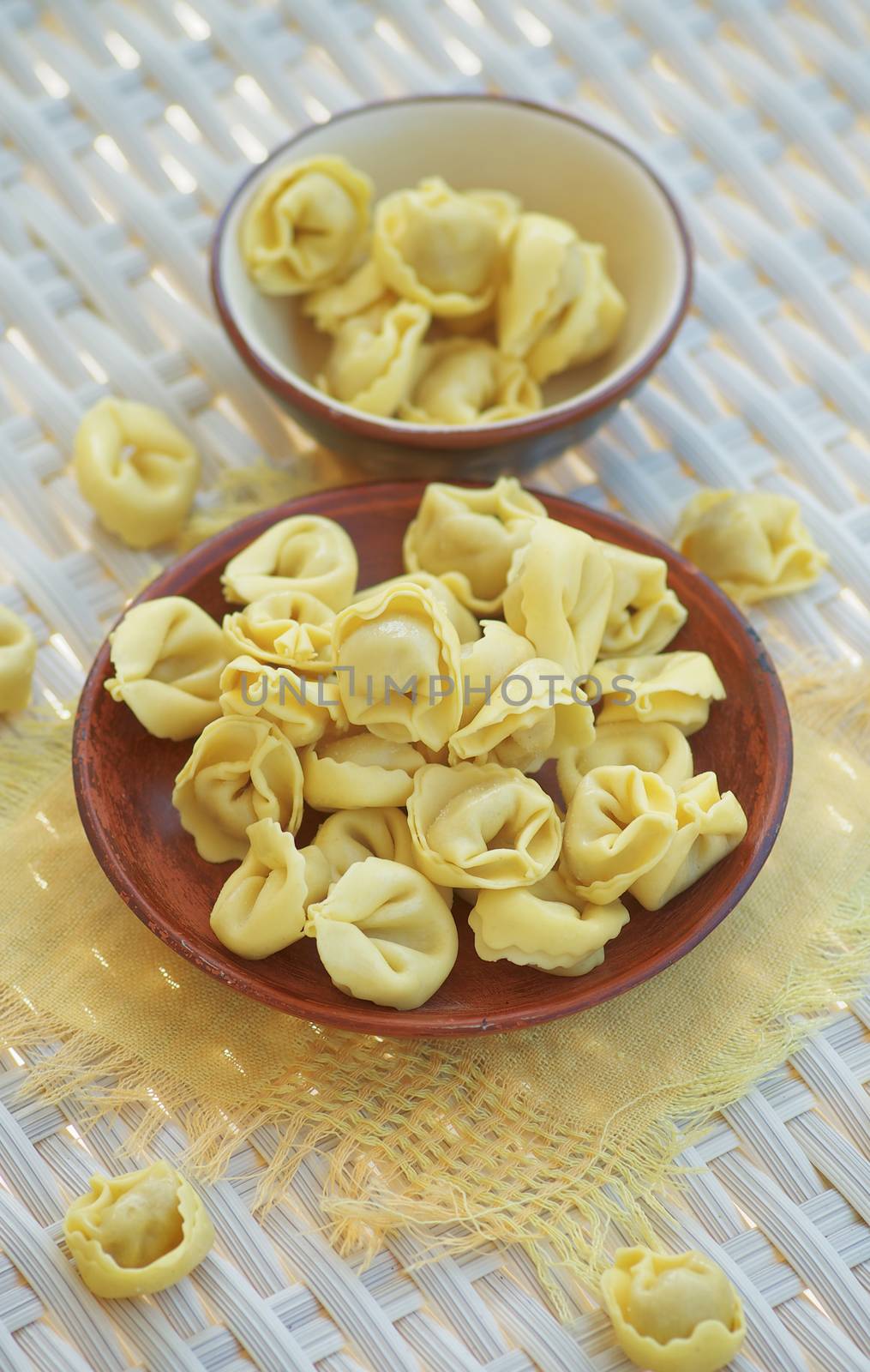Arrangement of Raw Meat Cappelletti in Brown Bowls with Yellow Napkin closeup on Wicker background. Focus on Foreground