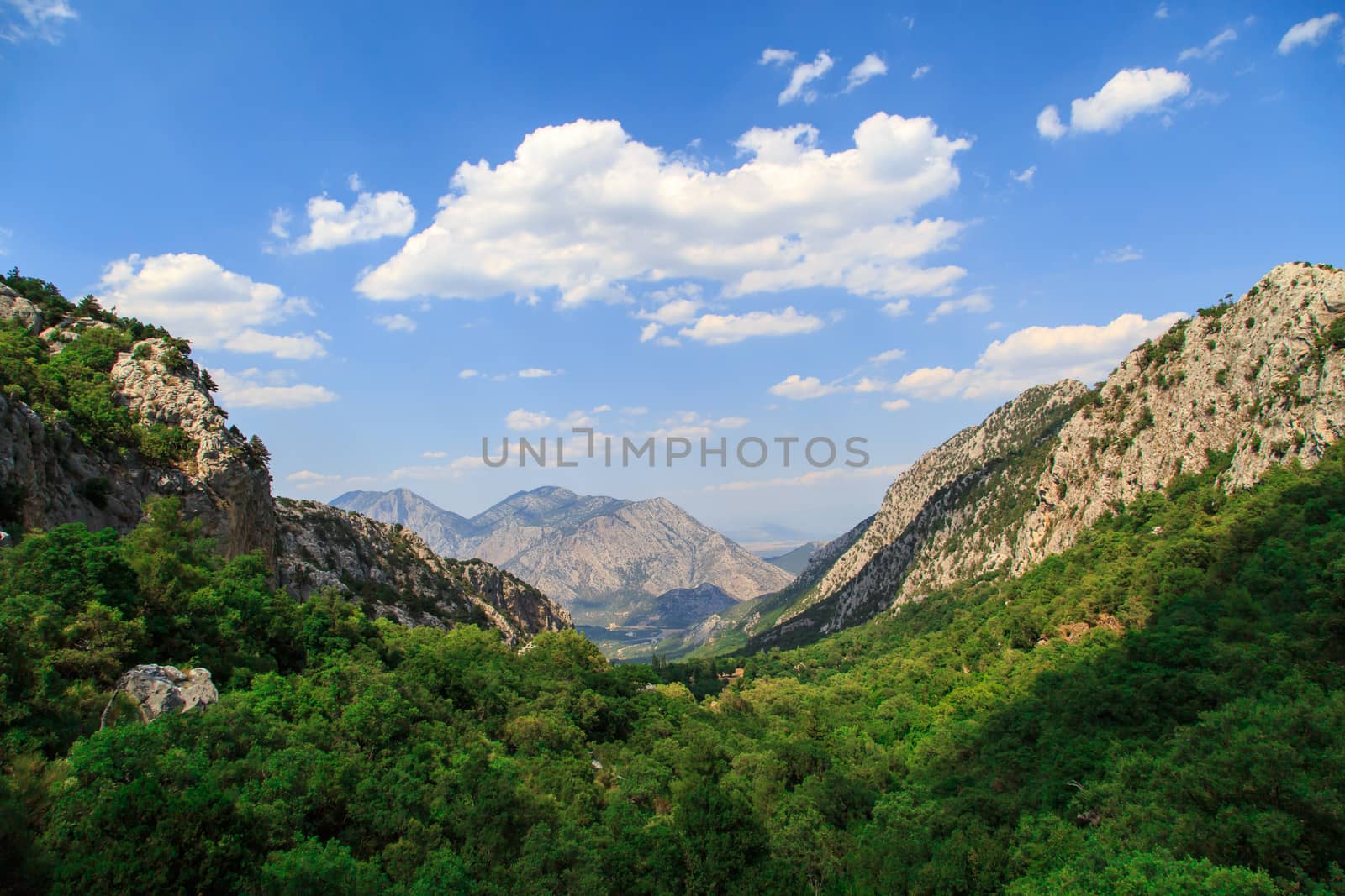 View of high mountains with small floiage around, on cloudy blue sky background.