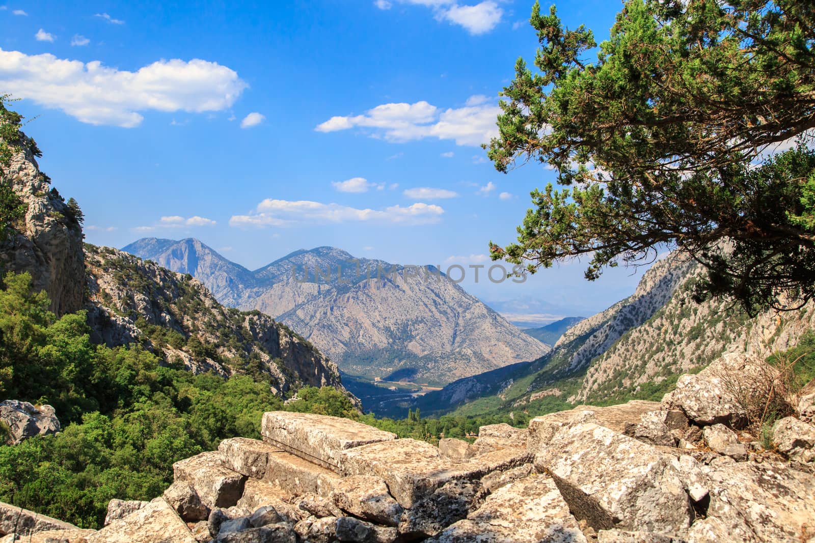 View of high mountains with small floiage and rocks around, on cloudy blue sky background.