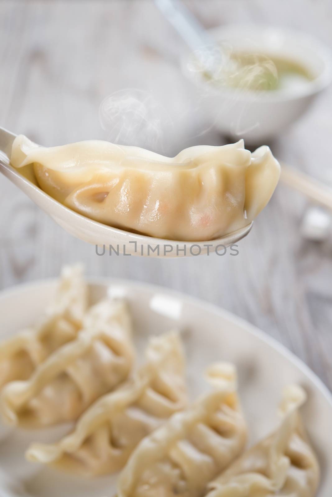 Fresh boiled dumpling on spoon with hot steams. Chinese food on old wooden background. 