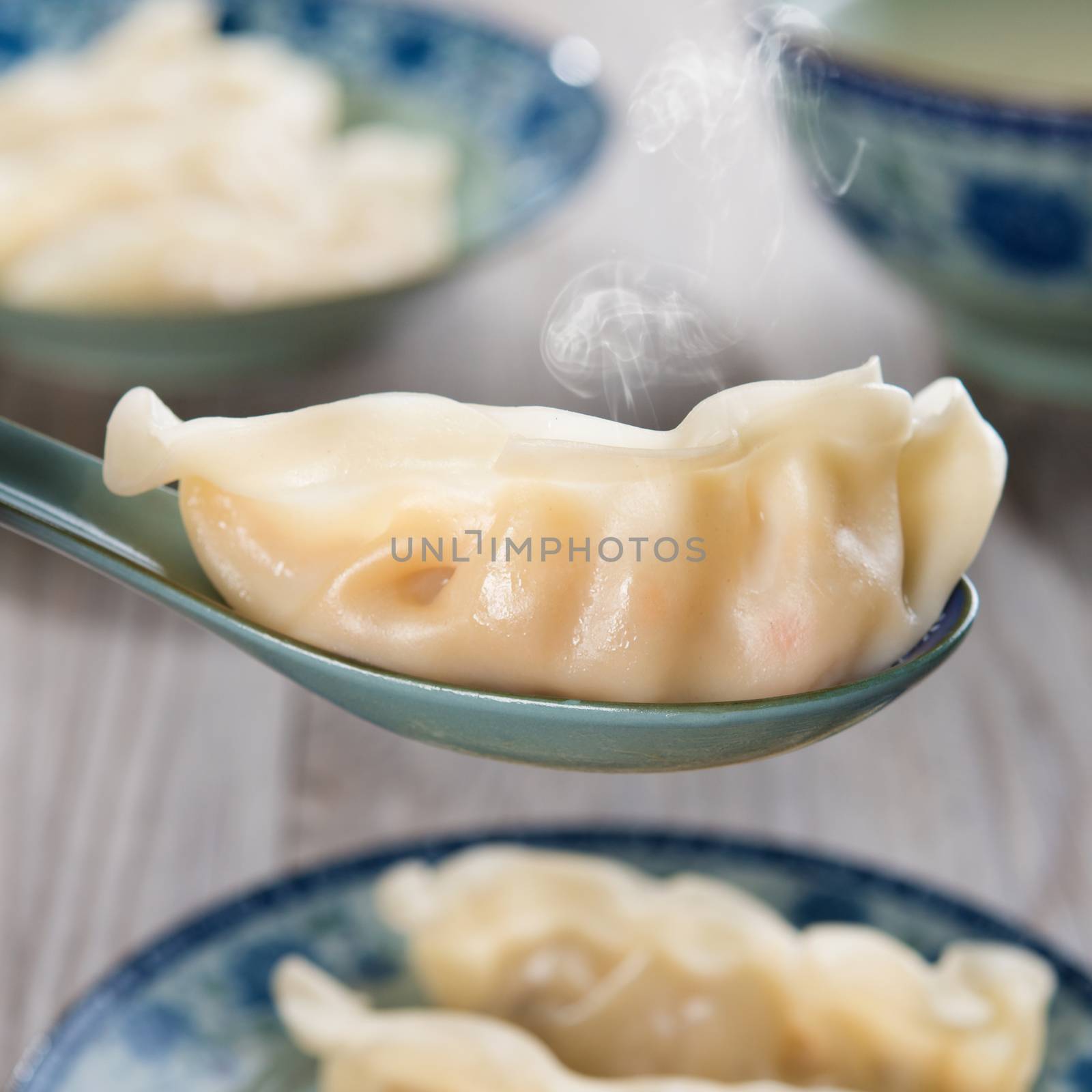 Close up fresh dumpling on spoon. Chinese cuisine on old wooden background. Fractal on the plate is generic print.