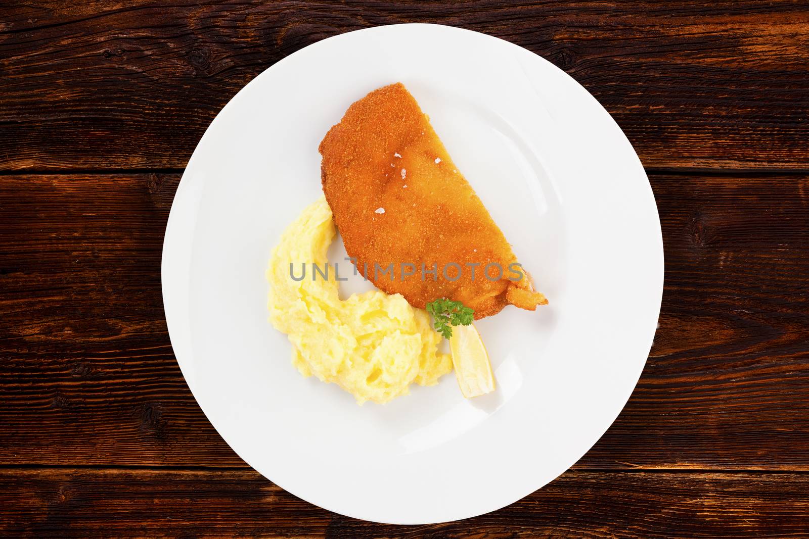 Delicious wiener schnitzel with mashed potatoes on plate on wooden background, top view. Traditional european cuisine.