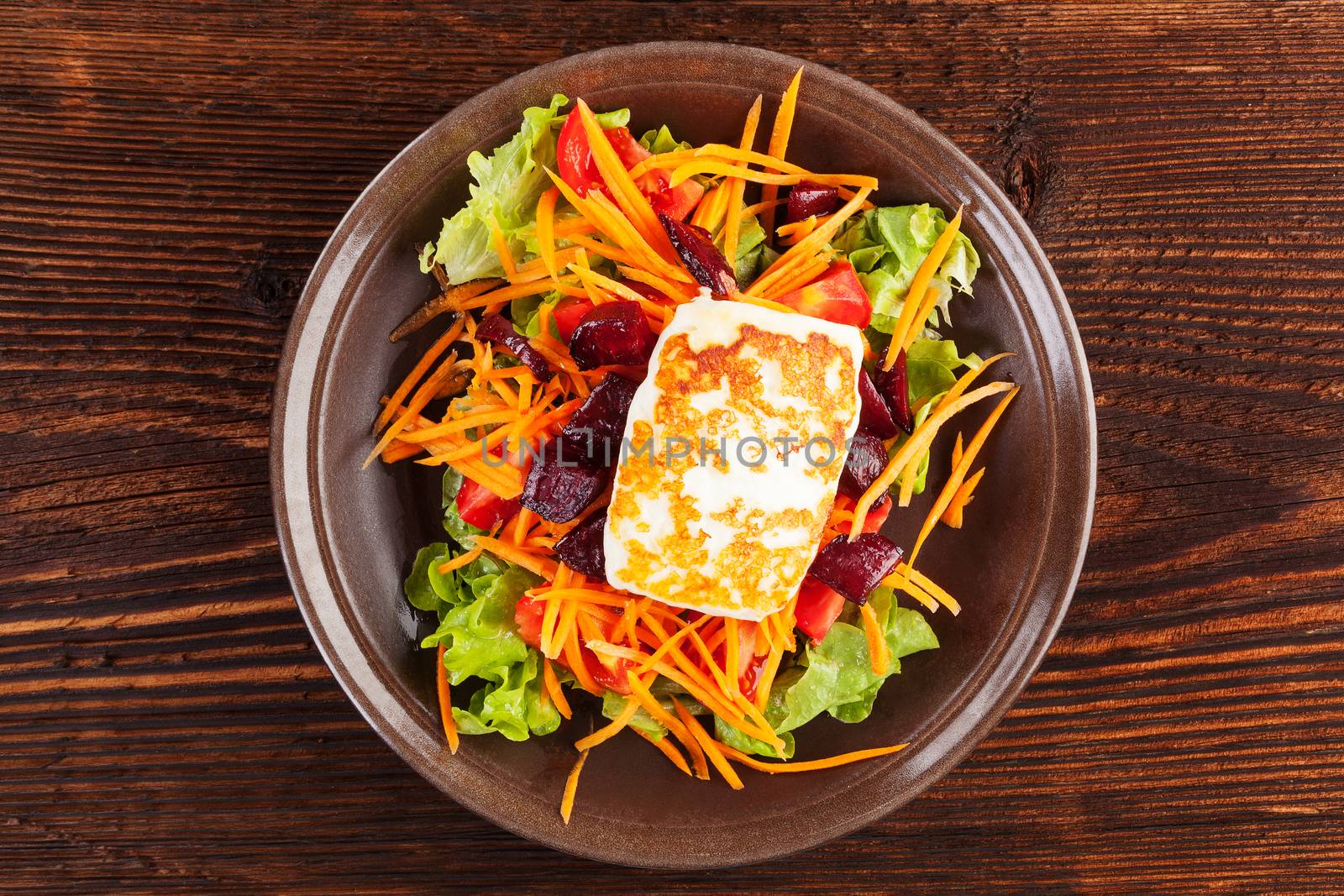 Grilled halloumi cheese with colorful fresh salad on plate on wooden table, top view. Culinary delicious vegetarian eating, mediterranean style.