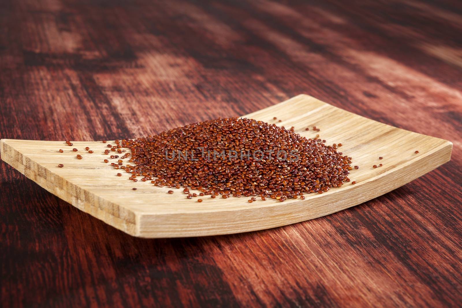 Red quinoa seeds on wooden plate on wooden background. 