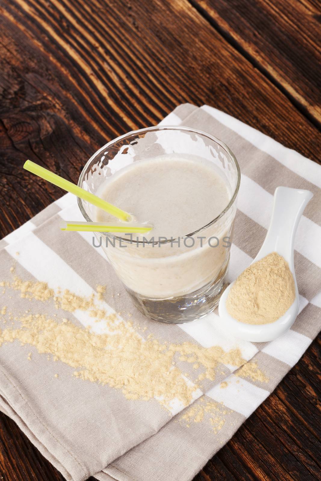 Maca powder on spoon and maca powder in milkshake on cloth on brown wooden table. Healthy living, alternative medicin, rustic styles. 