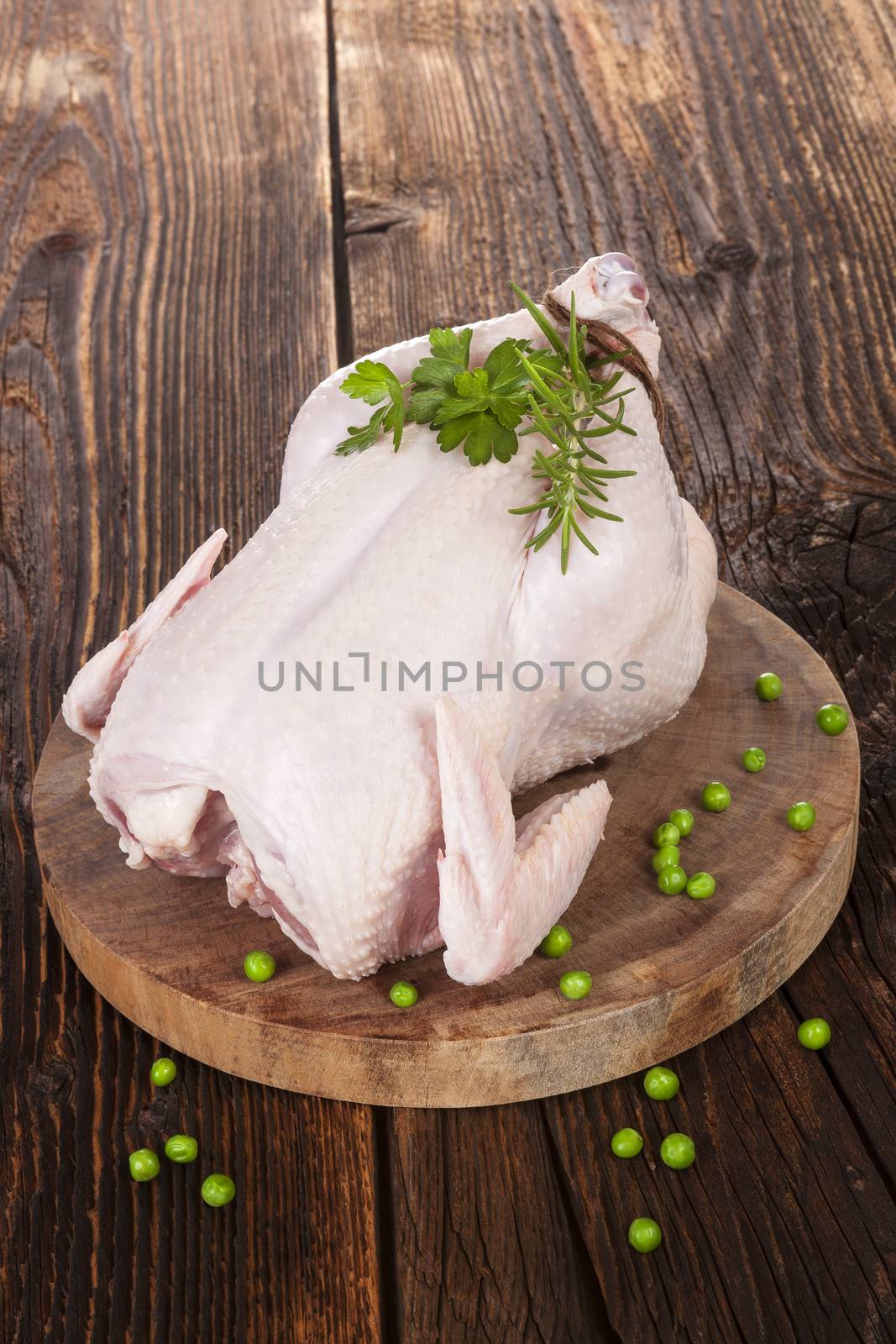Raw whole chicken with fresh herbs and peas on brown wooden textured background. Culinary white meat eating. Organic chicken. 