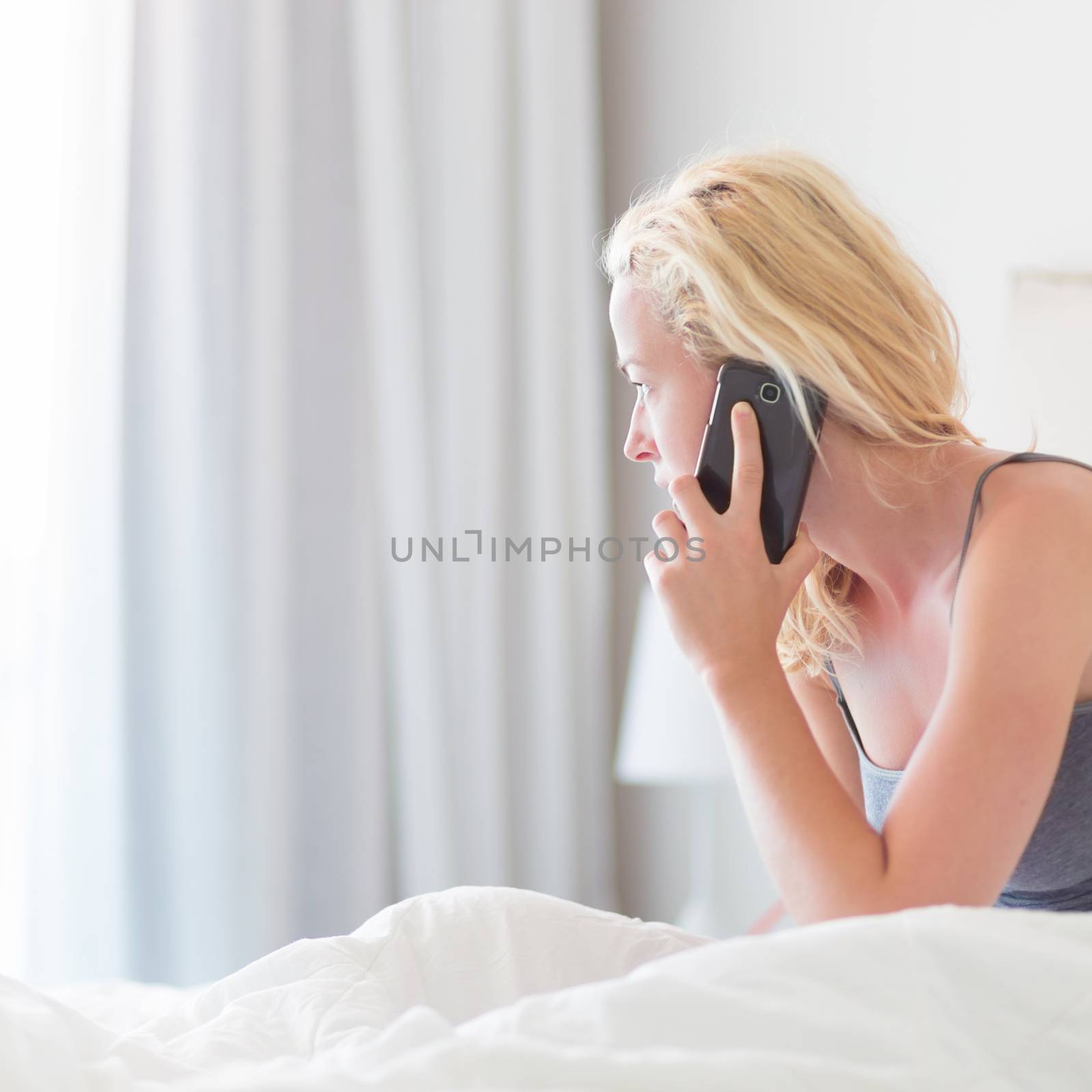 Woman talking by phone on bed in morning. by kasto