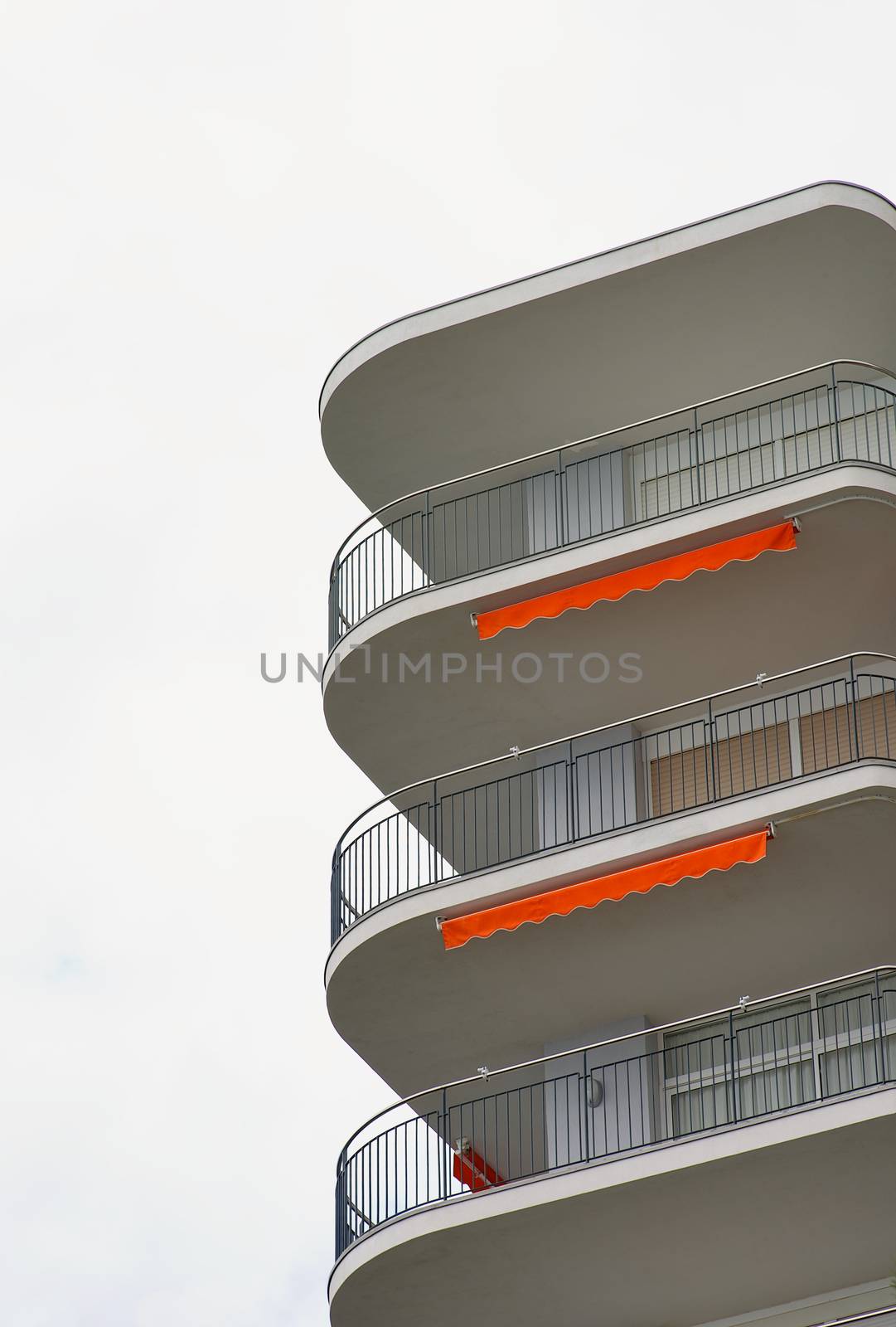 Modern Apartment Building with White Facade and Balcony with Orange Details closeup on Cloudy Sky background Outdoors