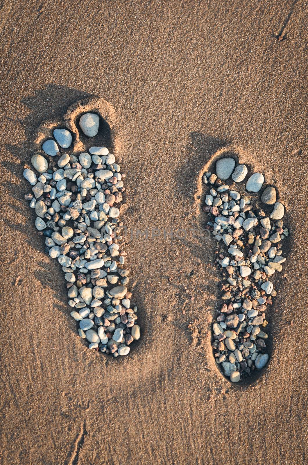 Bare feet made of pebble on the sandy beach