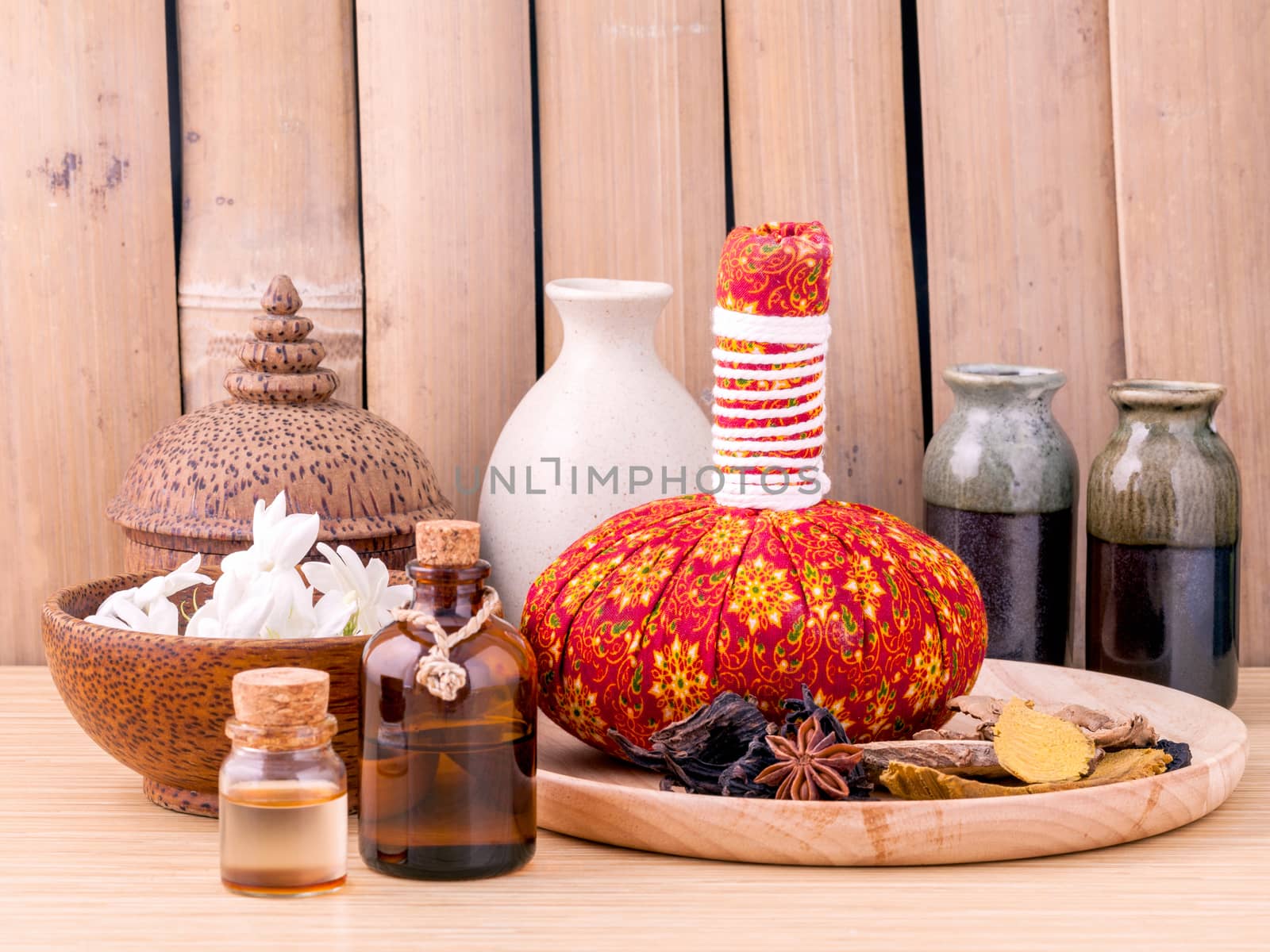 Natural Spa Ingredients herbal compress ball and essential Oil for alternative medicine and relaxation Thai Spa theme with bamboo background. by kerdkanno