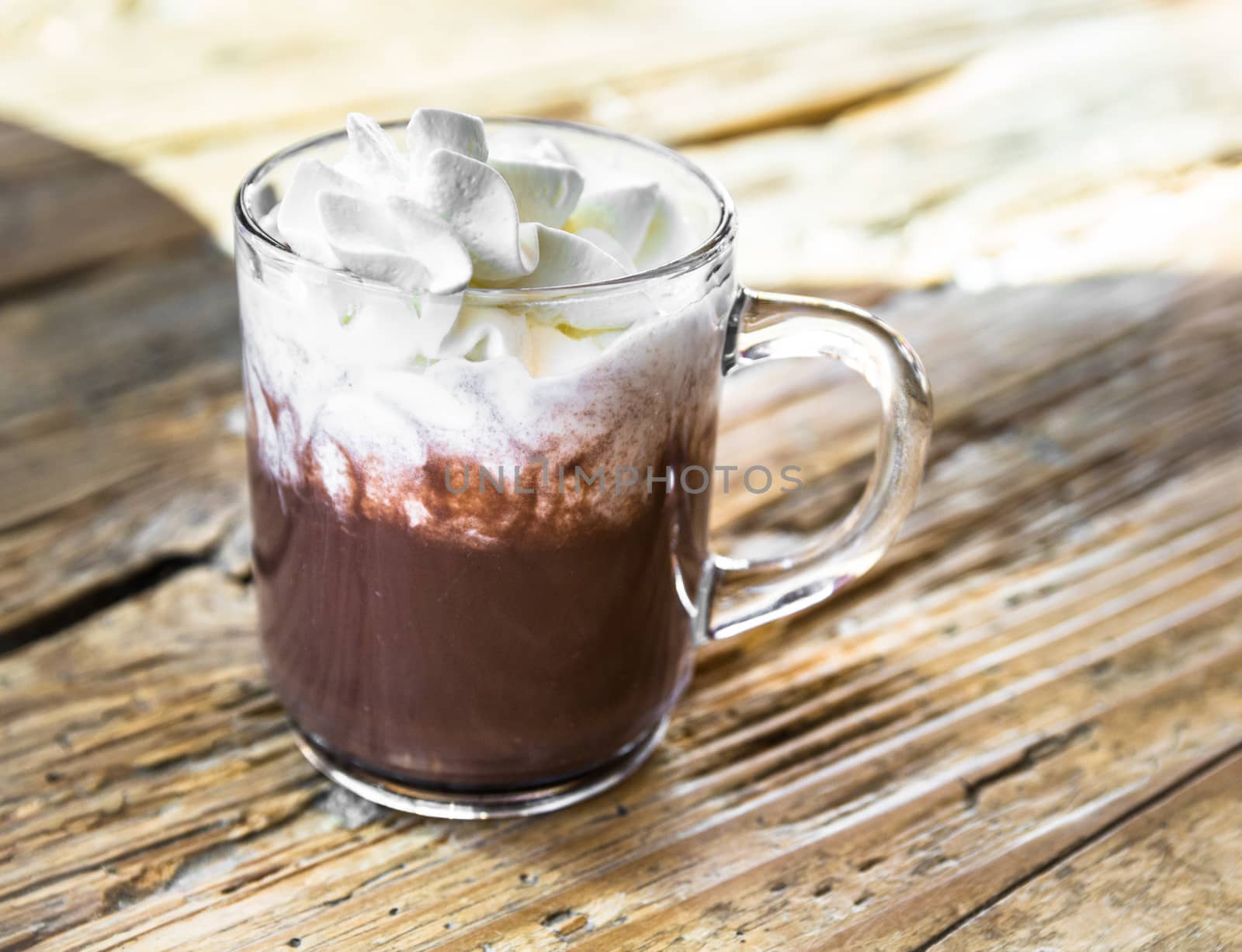 chocolate drink with whipped cream in transparent cup on rough wooden table