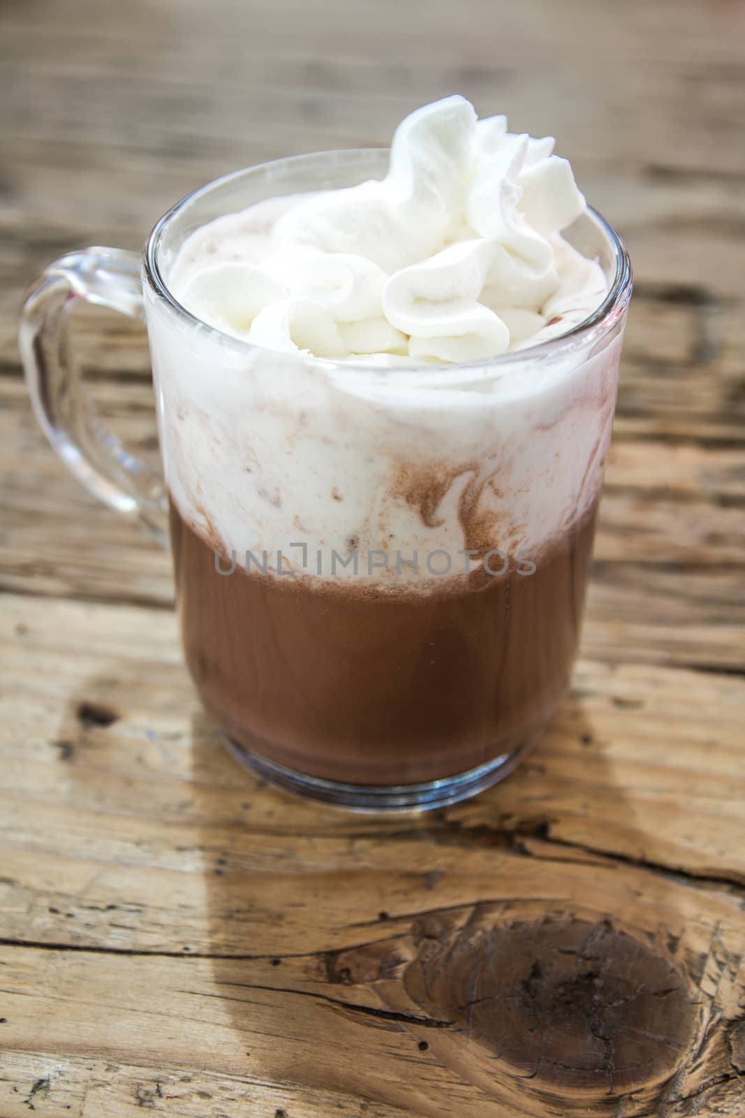 chocolate drink with whipped cream in transparent cup on rough wooden table