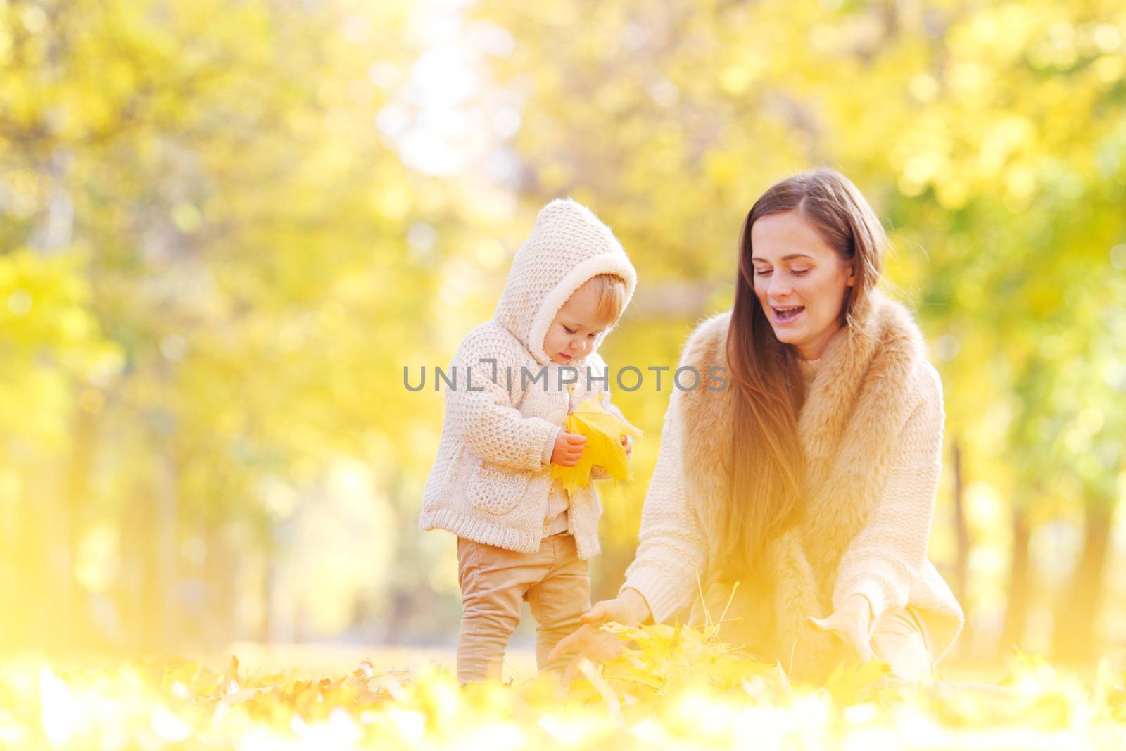 Mother and child having fun in autumn park among yellow leaves