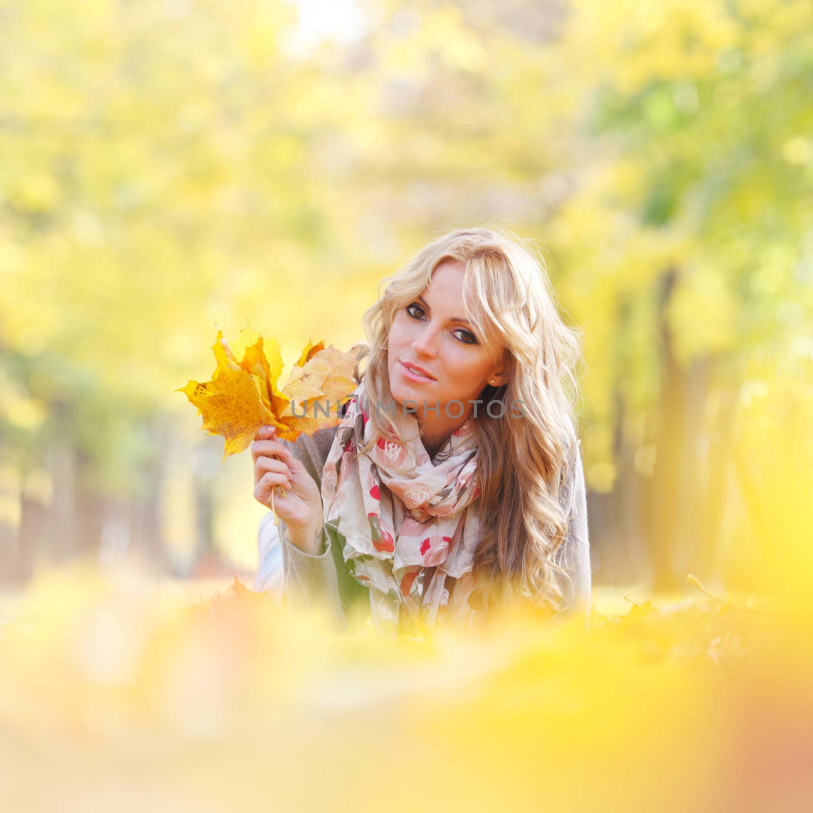 Portrait of a cute smiling woman lying in autumn leaves in park