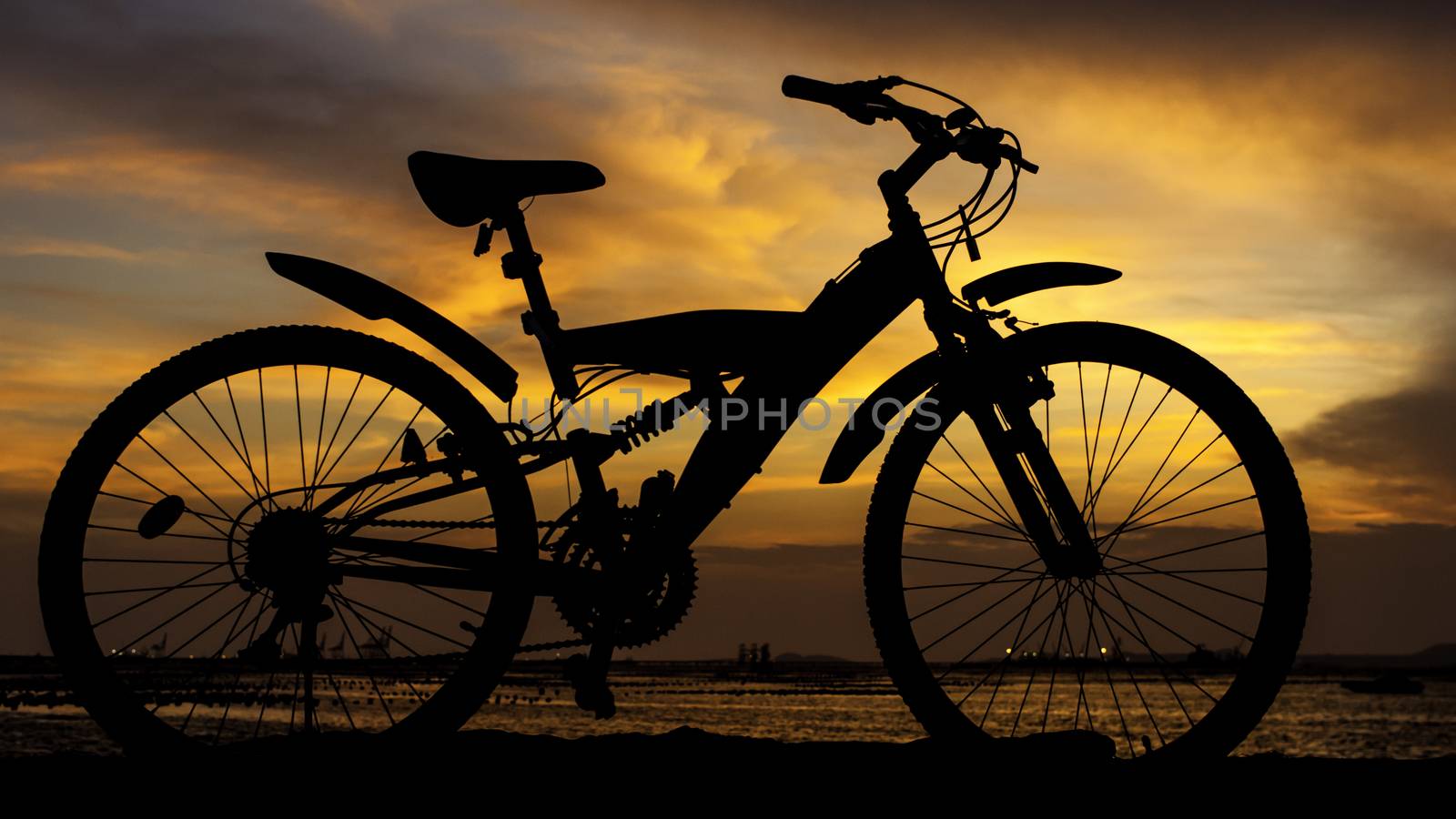 Silhouette of mountain bike with sunset sky beside sea, Thailand
