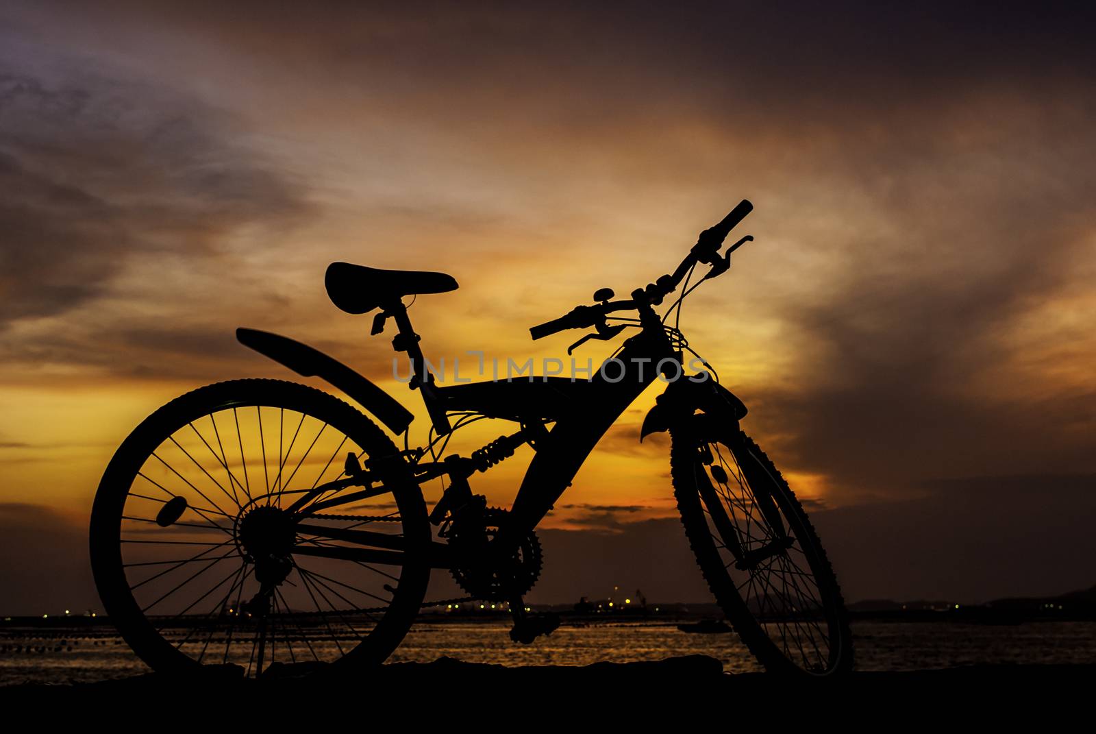 Silhouette of mountain bike parking on jetty beside sea with sunset sky background