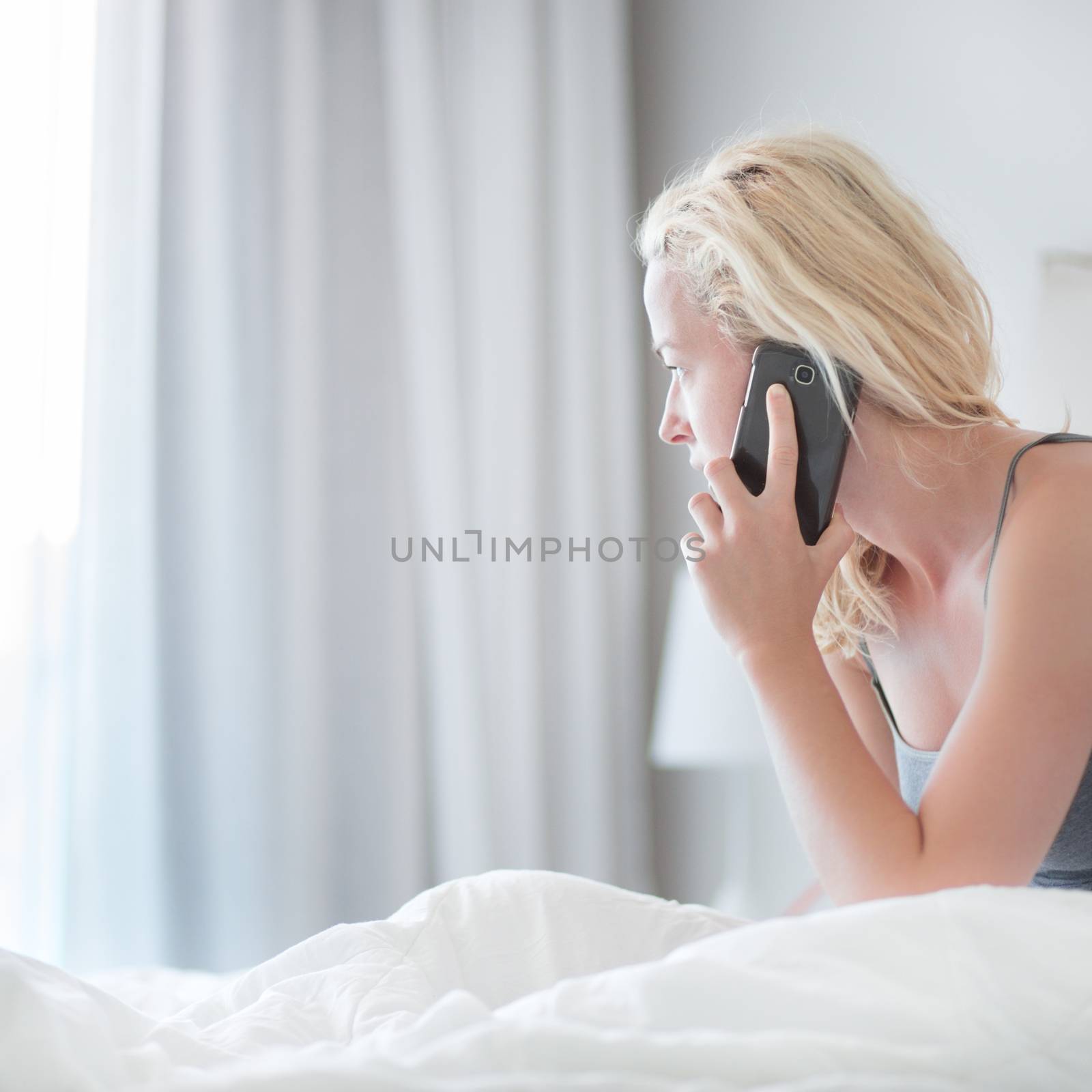 Portrait of  young lady with mobile phone in bed at home. Tired sleepy woman receiving emergency call in bed early in the morning.