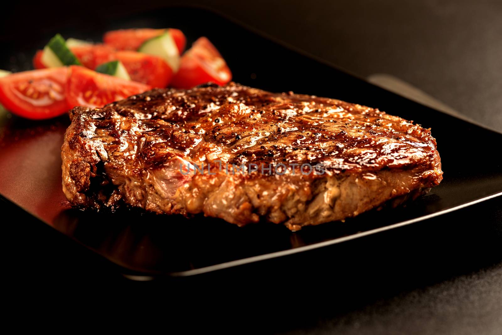 Grilled steak and vegetables on black plate macro by Nanisimova