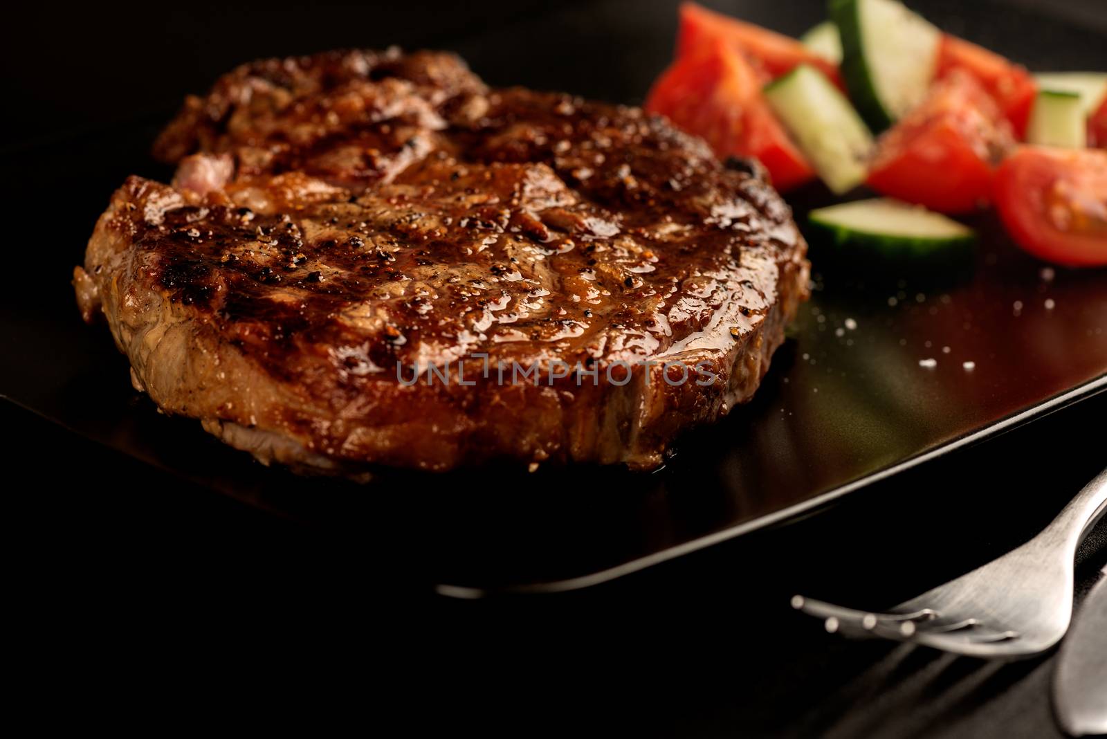 Grilled steak and vegetables on black plate with fork by Nanisimova