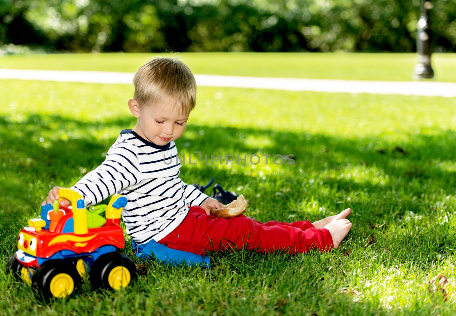 Little preschool boy playing with big toy car at city park by Nanisimova