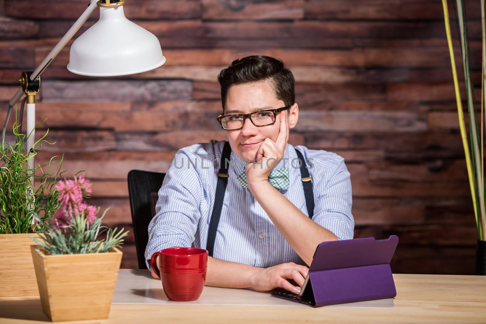 Wondering dapper female in suspenders at desk with grin