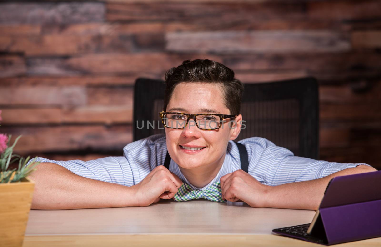 Boyish woman pulling bowtie while leaning on desk