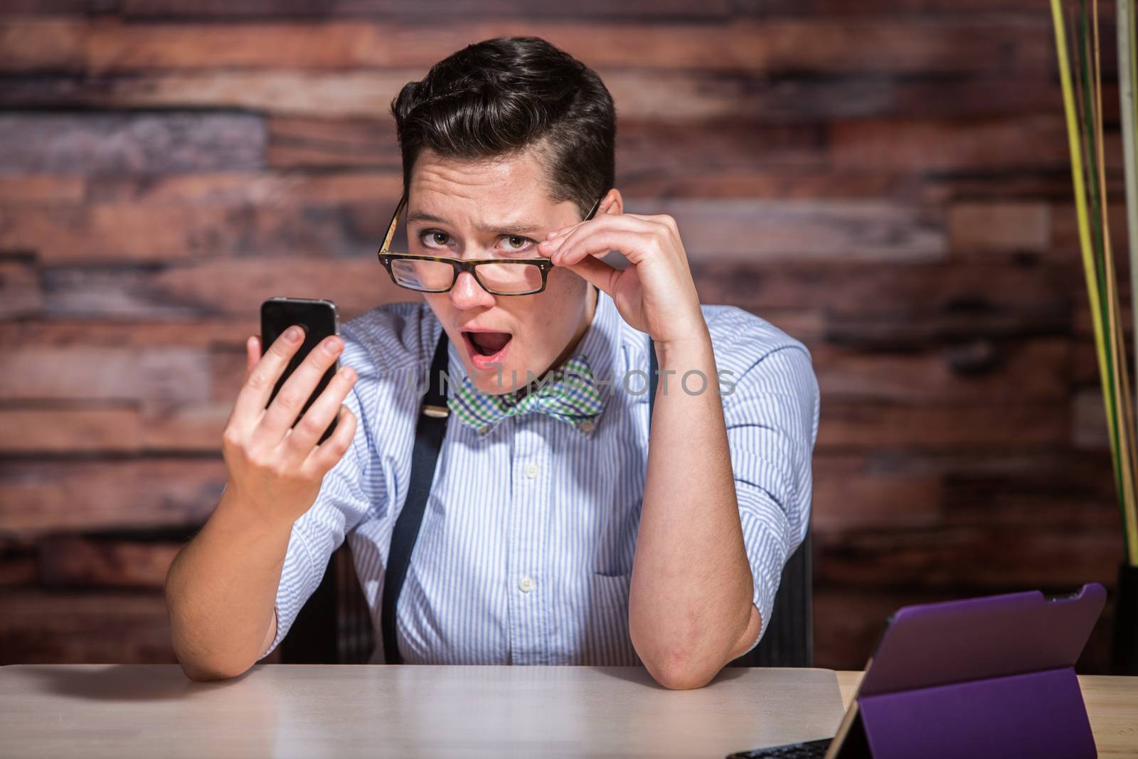 Insulted boyish woman holding eyeglasses and looking at phone