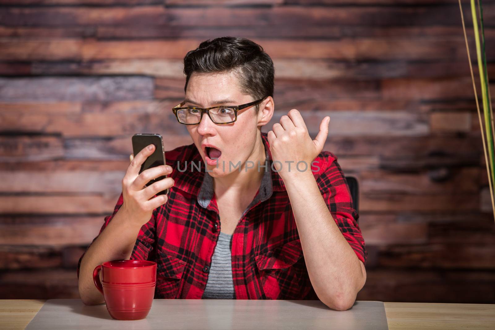 Surprised boyish woman in flannel shirt on smart phone