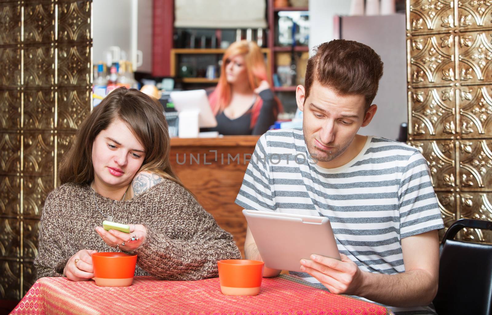 Young couple with phone and tablet computer in cafe