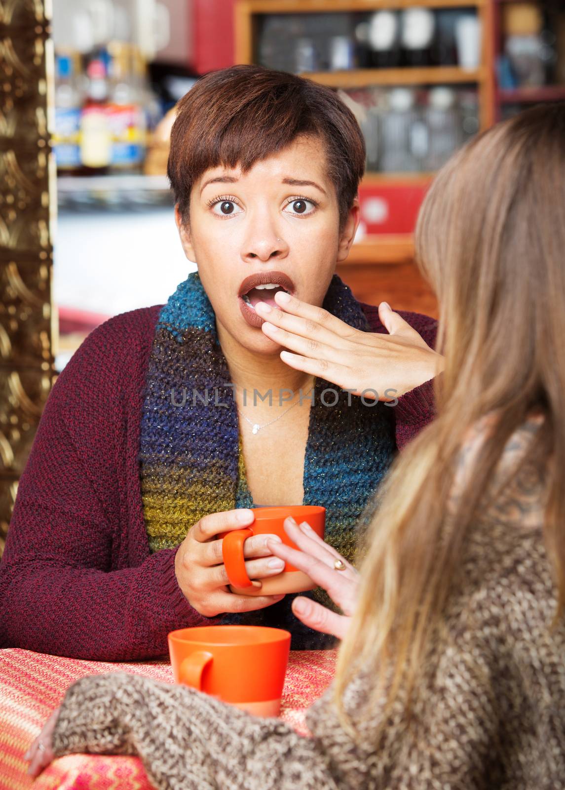 Shocked woman with hand covering mouth at coffee house