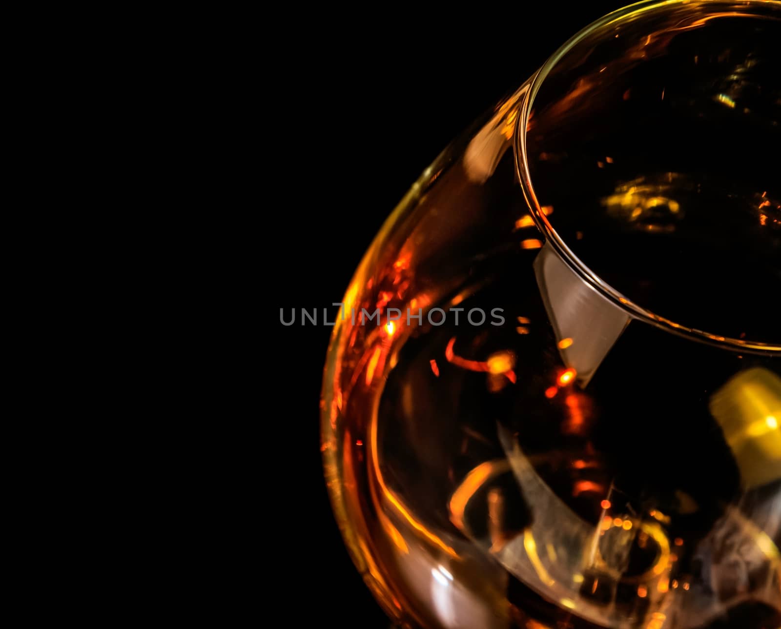 top of view of snifter of brandy in elegant typical cognac glass on black background with red reflection, with light tint red