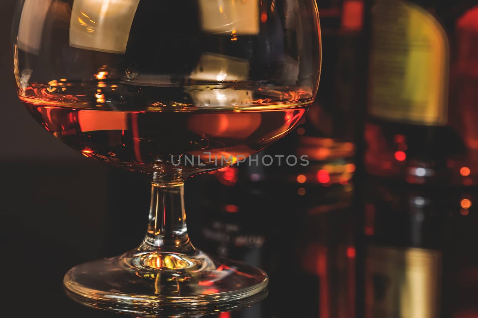 snifter of brandy in elegant typical cognac glass  in front of bottles in background, warm atmosphere