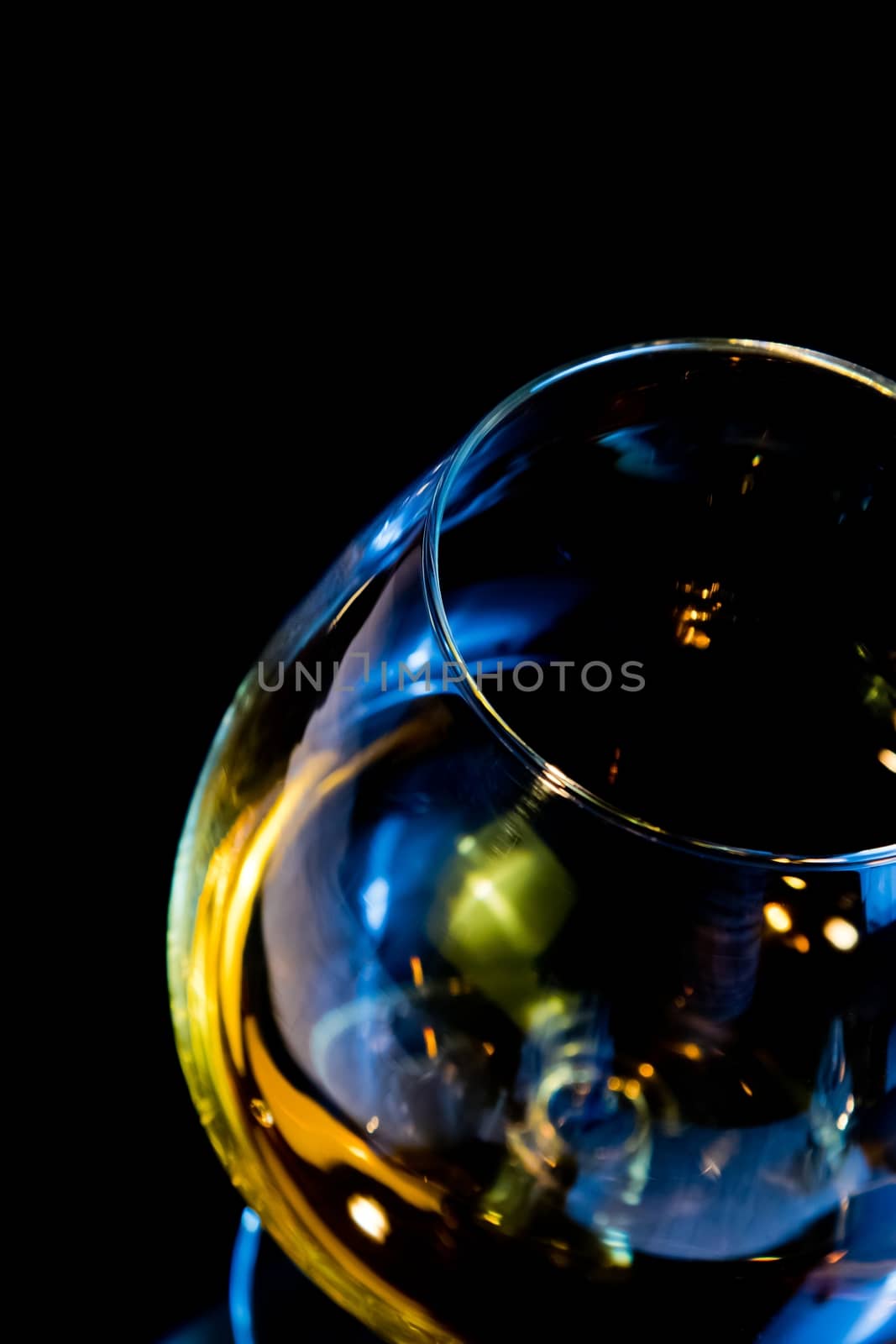 top of view of snifter of brandy in elegant typical cognac glass on black background with red reflection, with light tint red