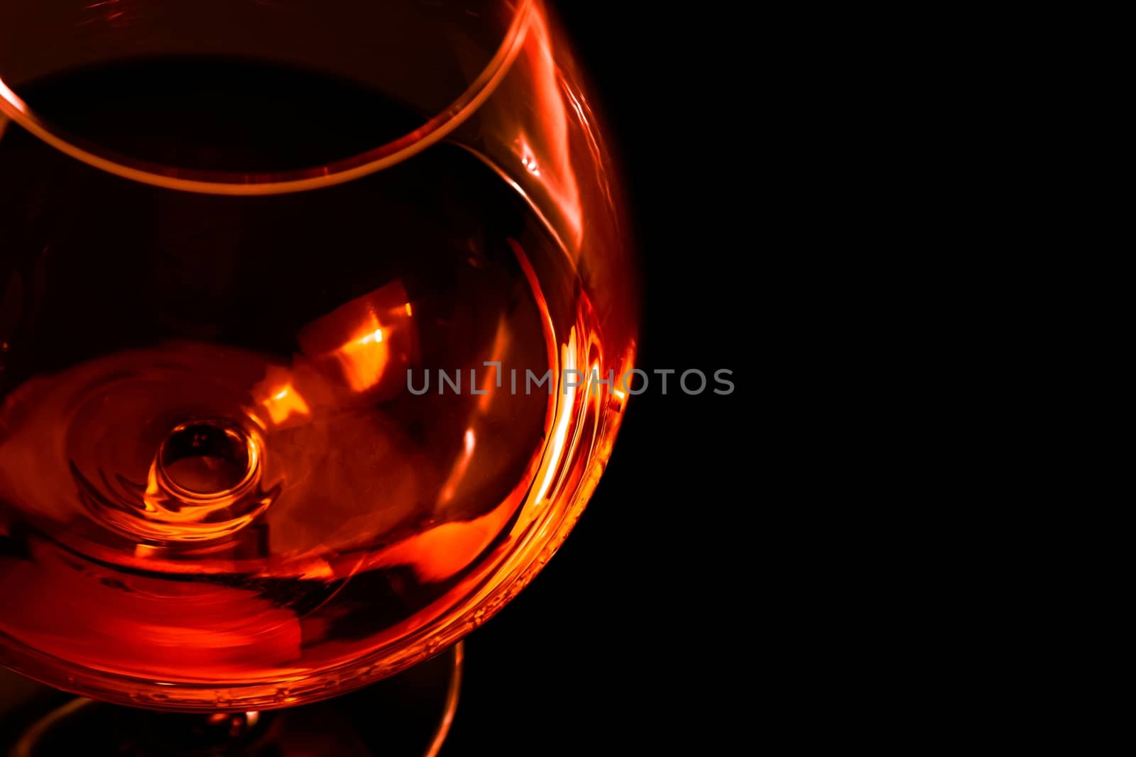 top of view of snifter of brandy in elegant typical cognac glass on black background with red and orange reflection