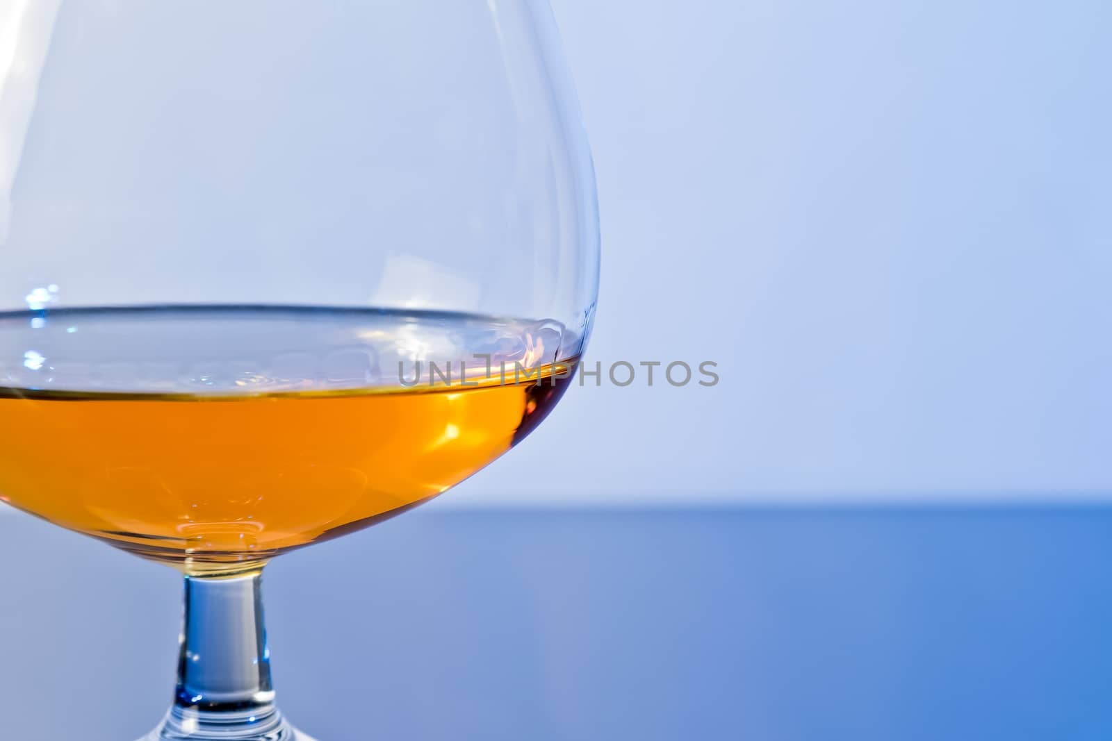 snifter of brandy in elegant typical cognac glass on blue light background, with reflection
